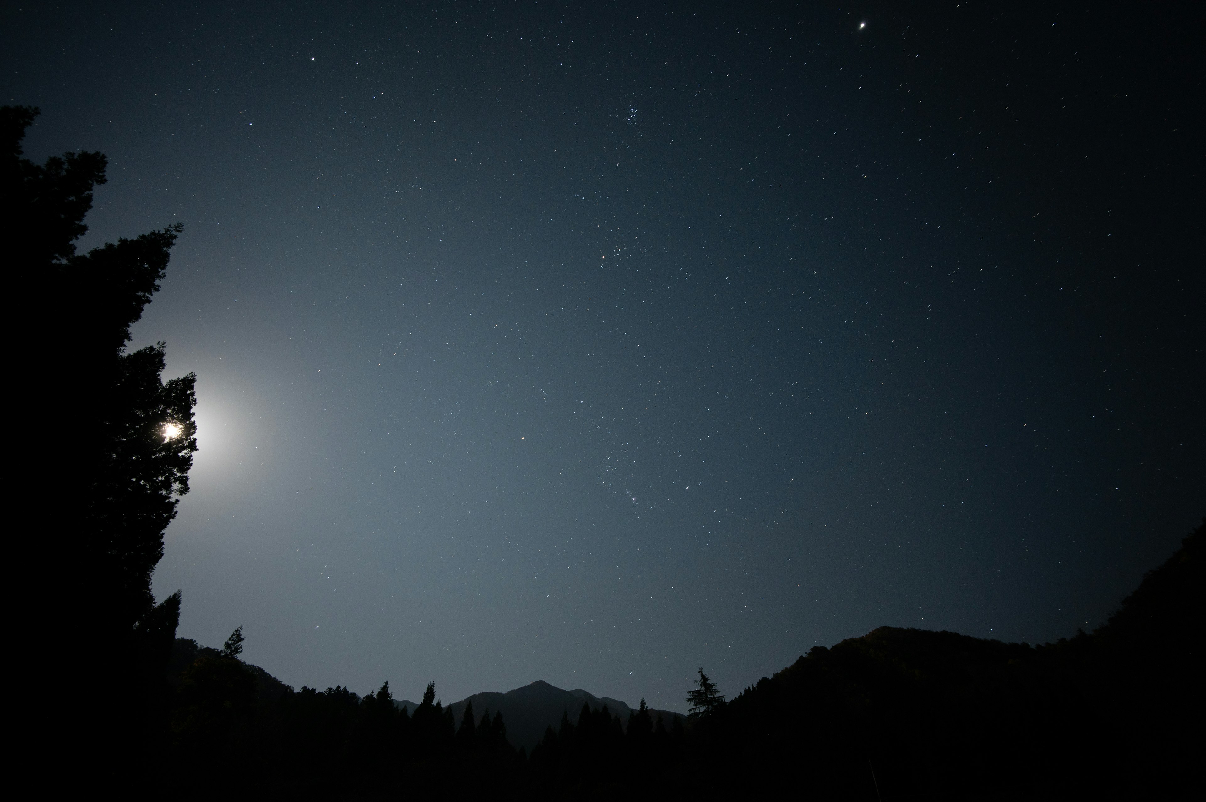 Silhouette of mountains under a starry night sky illuminated by moonlight