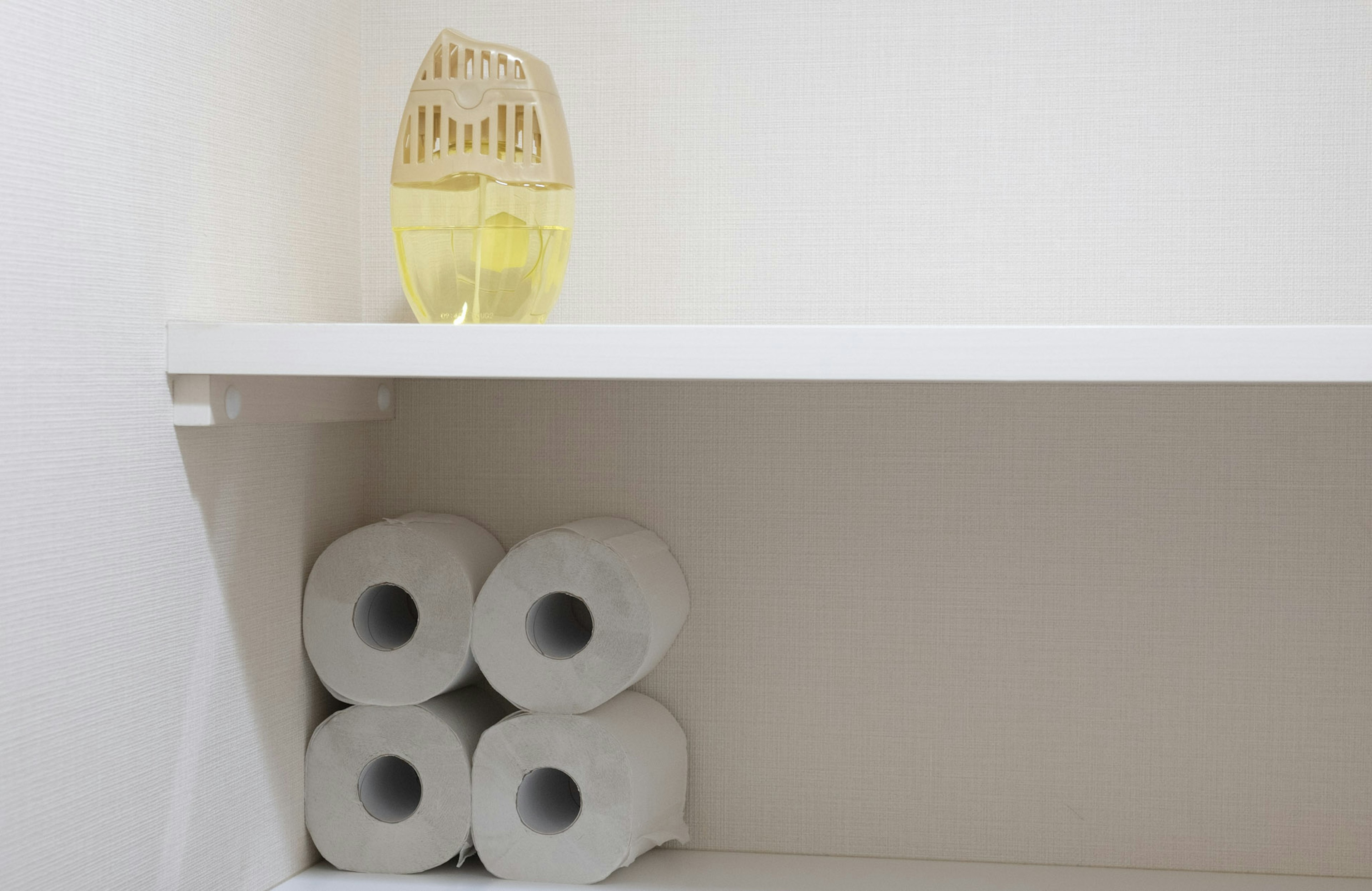 Un diffuseur jaune sur une étagère avec des rouleaux de papier toilette bien rangés en dessous