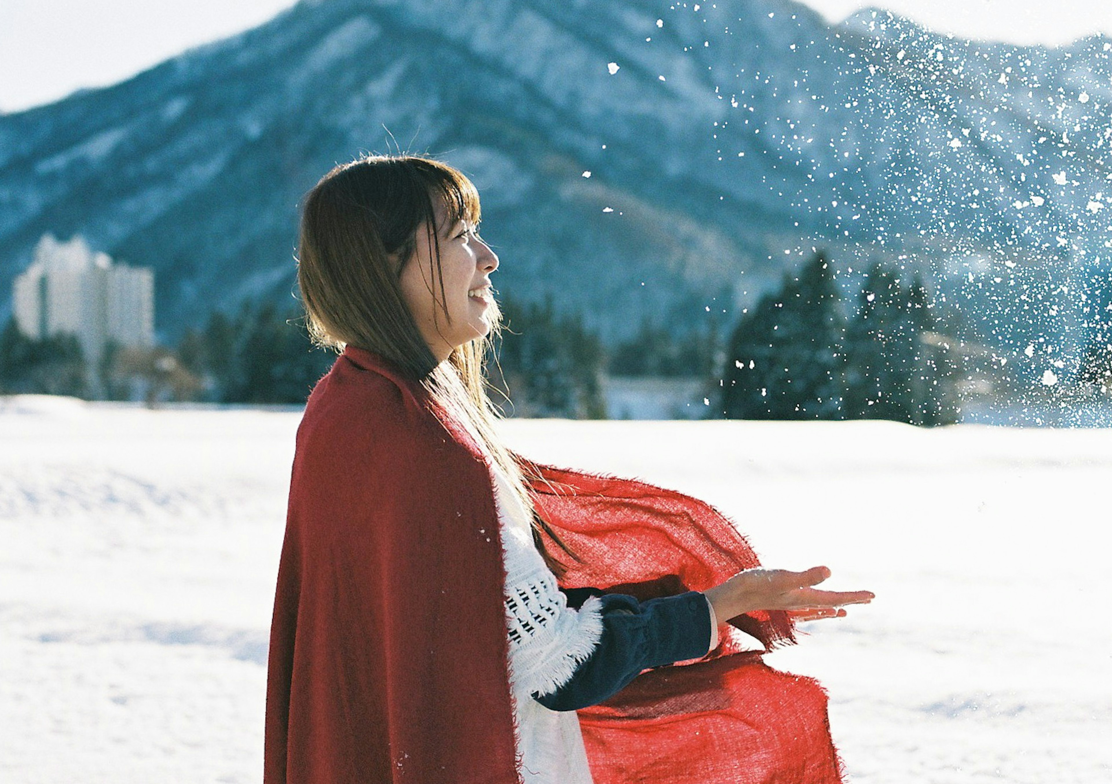 Une femme en manteau rouge se tient dans la neige avec des montagnes en arrière-plan