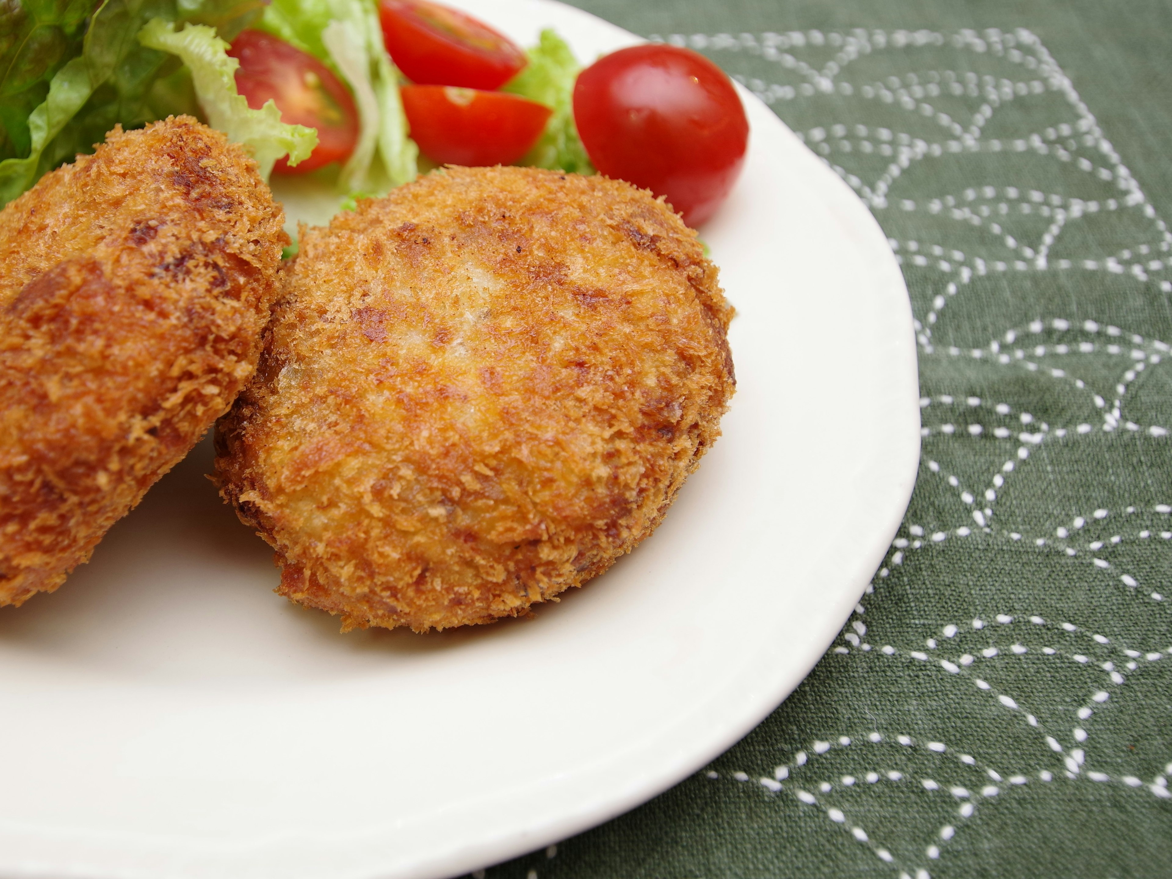 Dua kroket renyah disajikan dengan salad dan tomat ceri