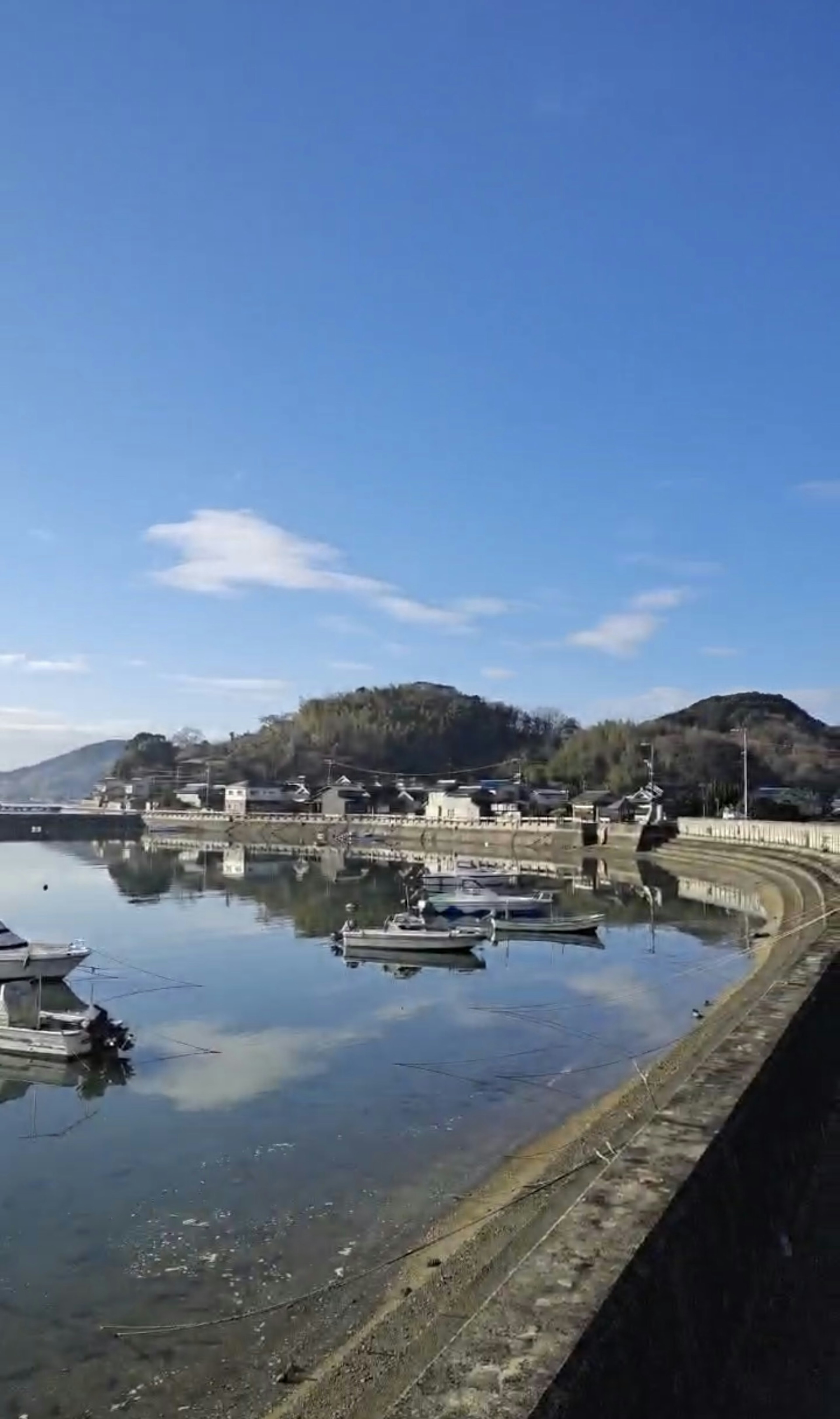 Serene coastal landscape with blue sky and calm waters featuring moored boats and hills