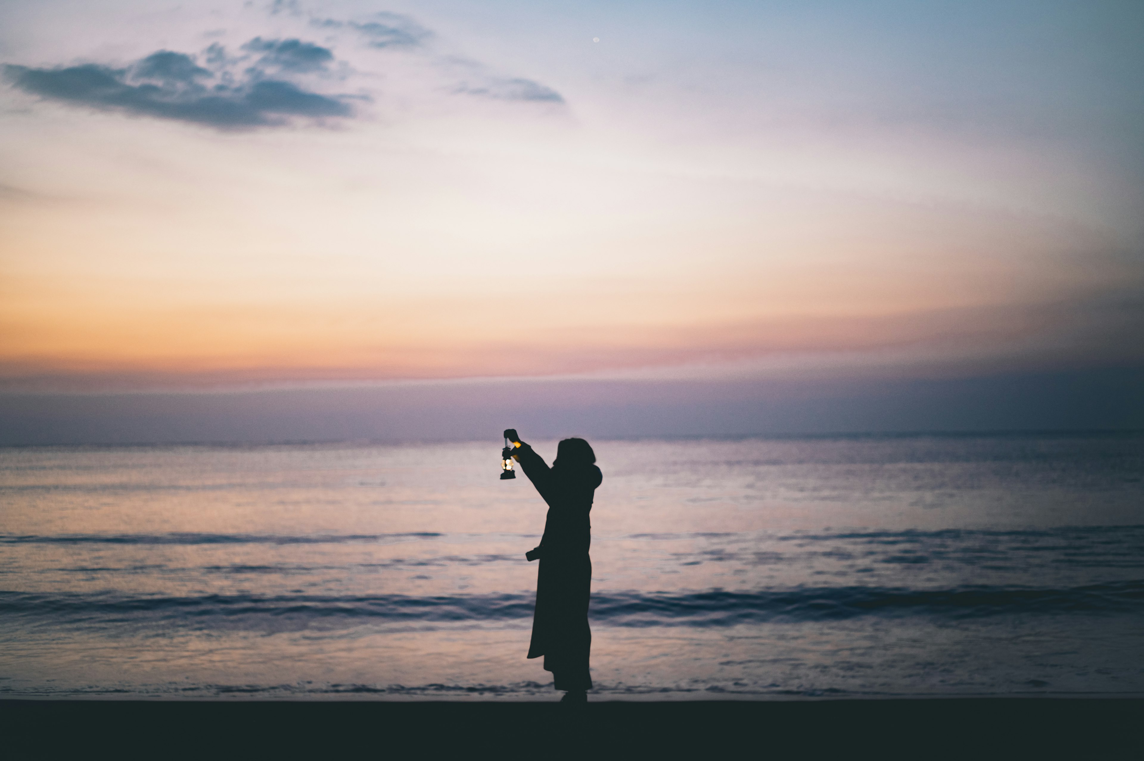 海辺で夕日を背景に立つ女性のシルエット