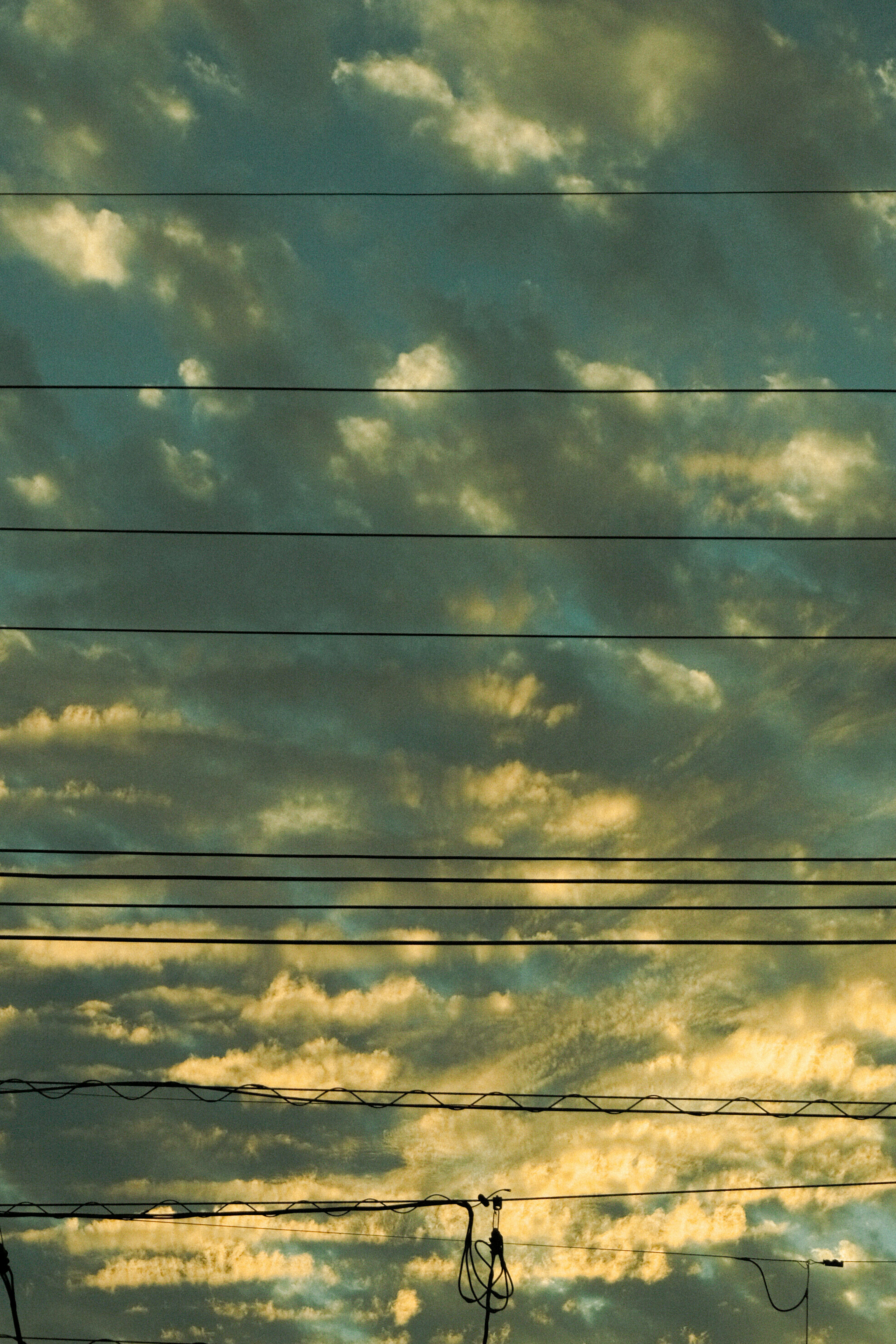 青と黄色の雲が広がる空に電線が見える風景