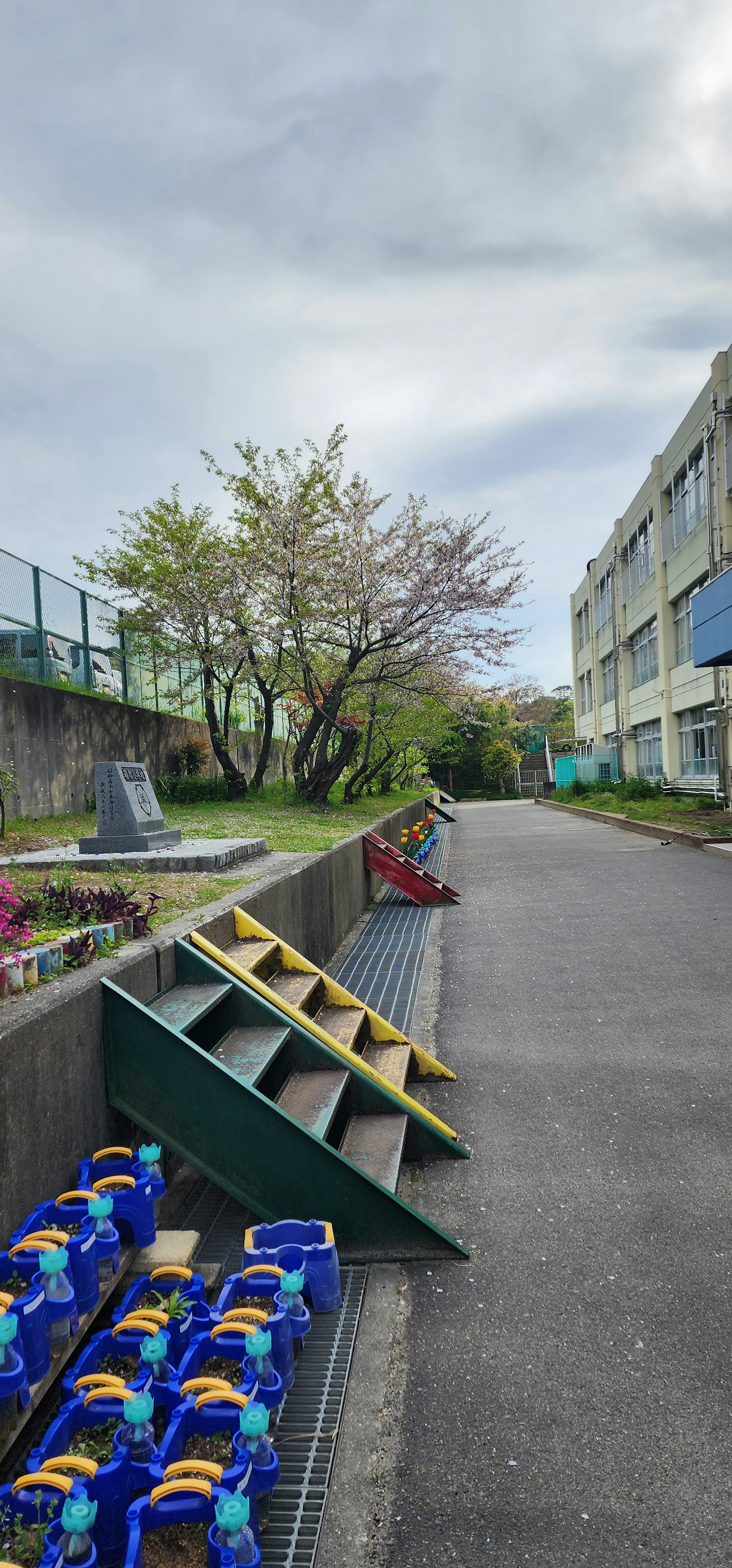 学校の通路に並ぶカラフルなバケツと階段のある風景