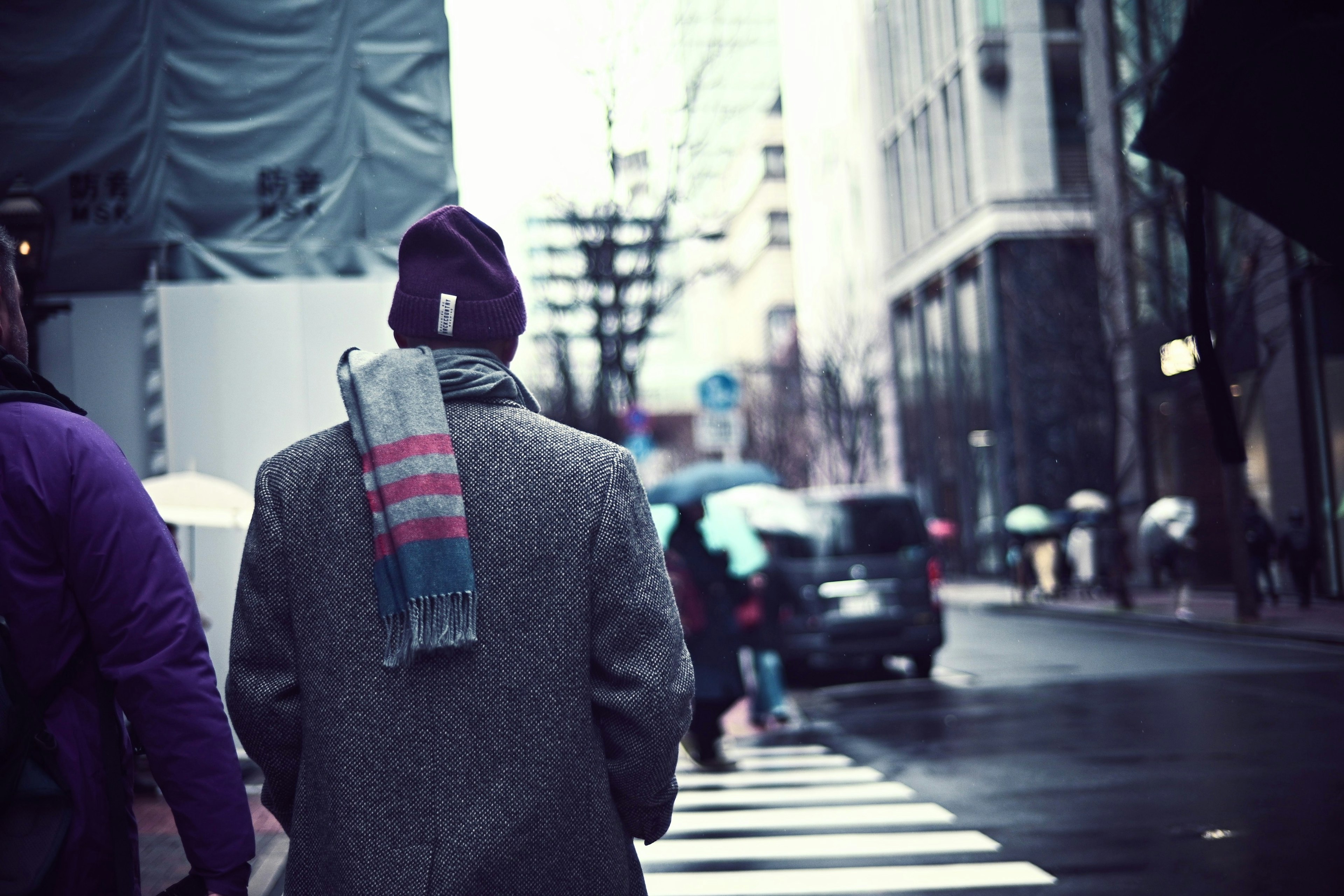 Uomo che cammina in una strada di città con un cappotto e un berretto e una sciarpa a righe