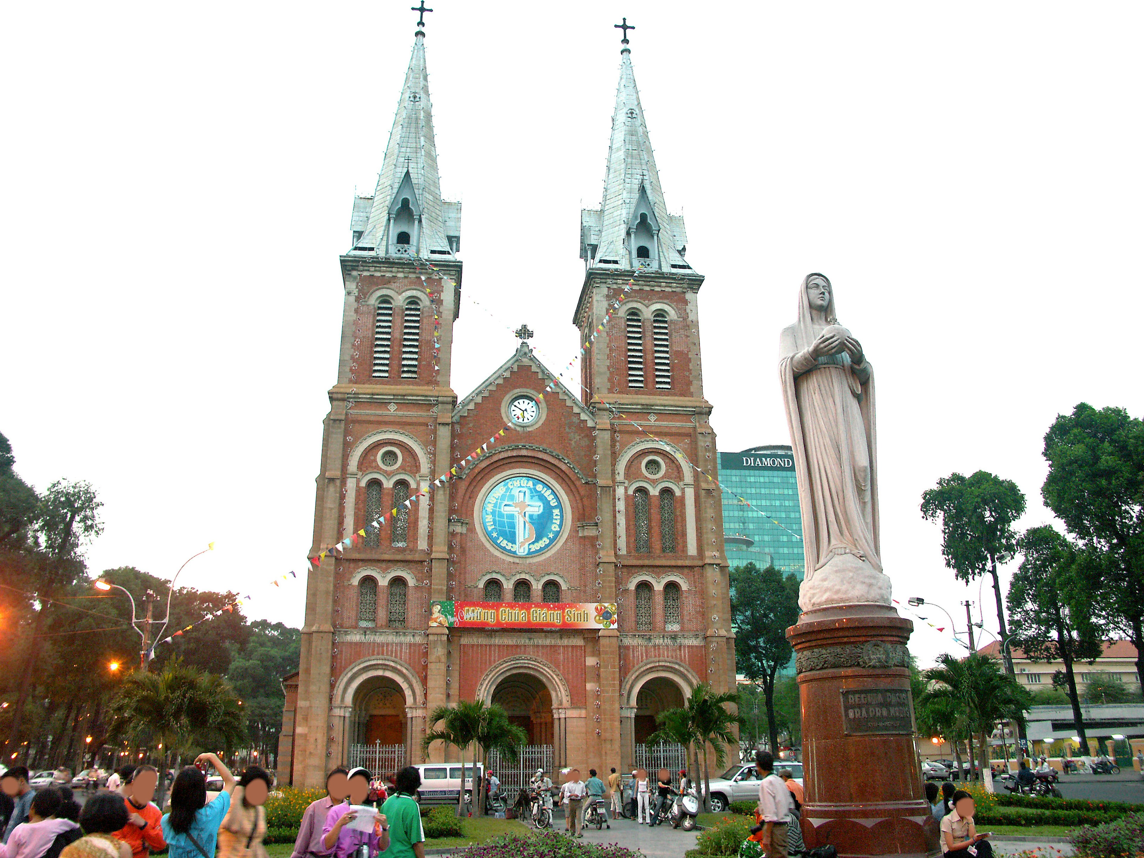 Gens devant la belle cathédrale en briques rouges de Saïgon avec ses flèches