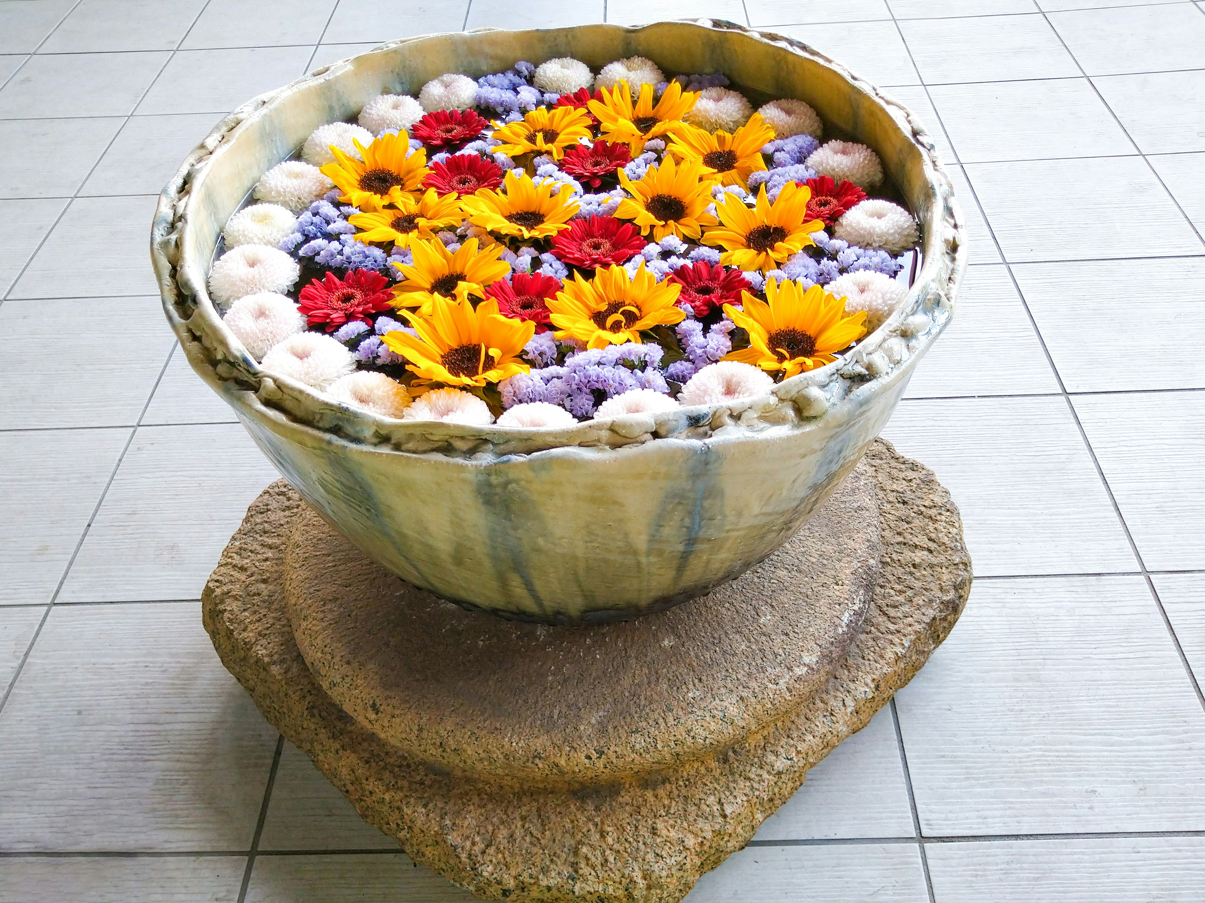 A large bowl filled with colorful flowers placed on the floor