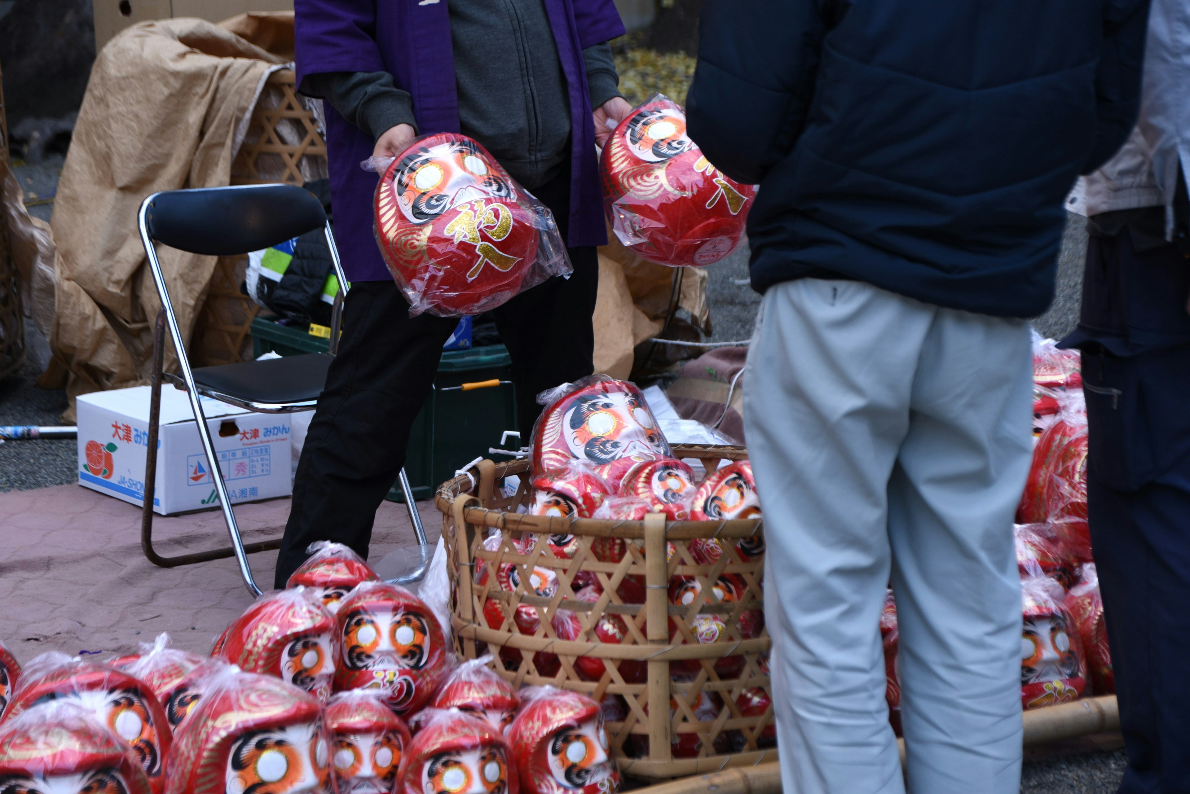 Personas interactuando con muñecas Daruma rojas en un mercado