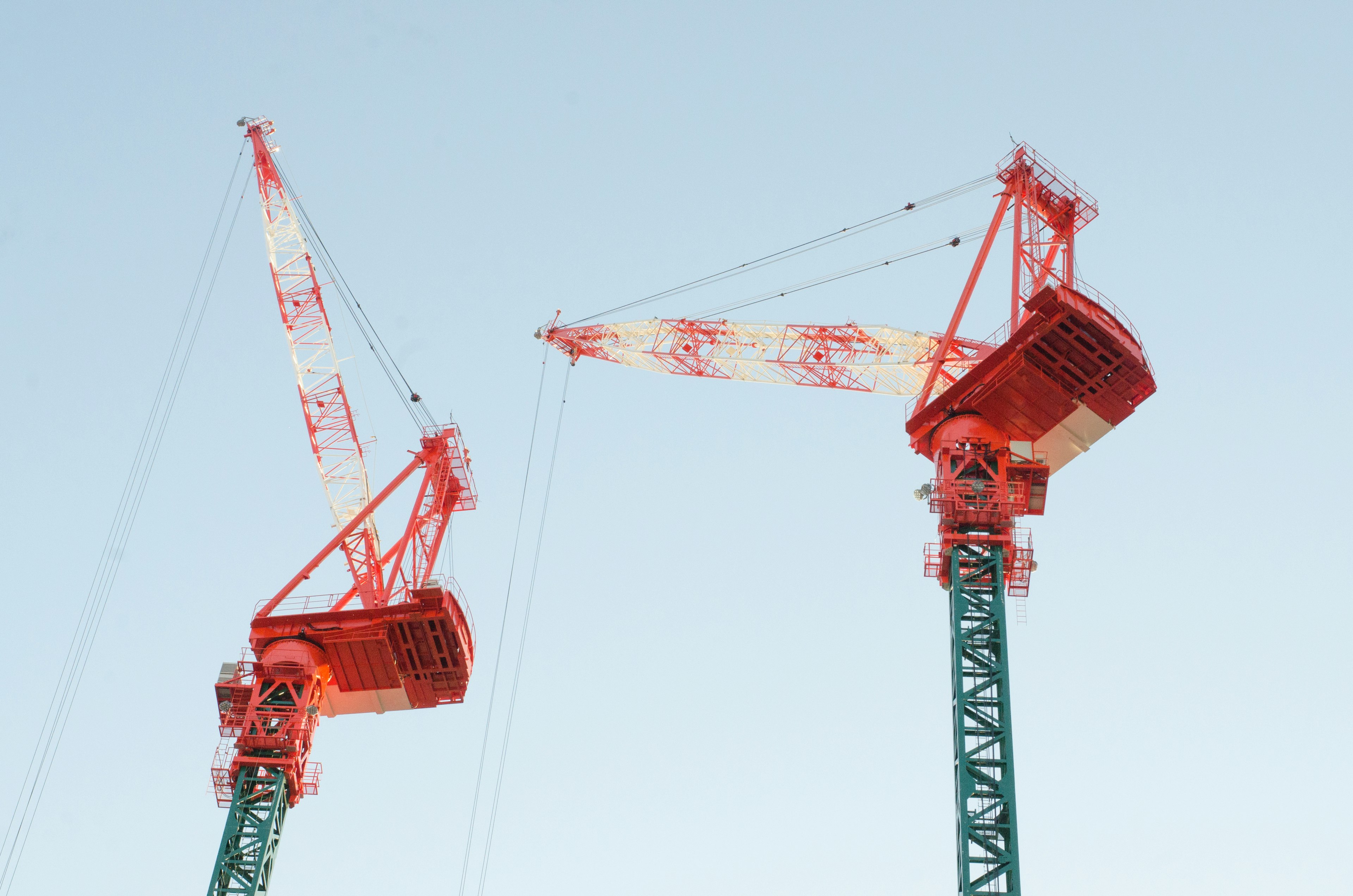 Two red cranes standing under a blue sky