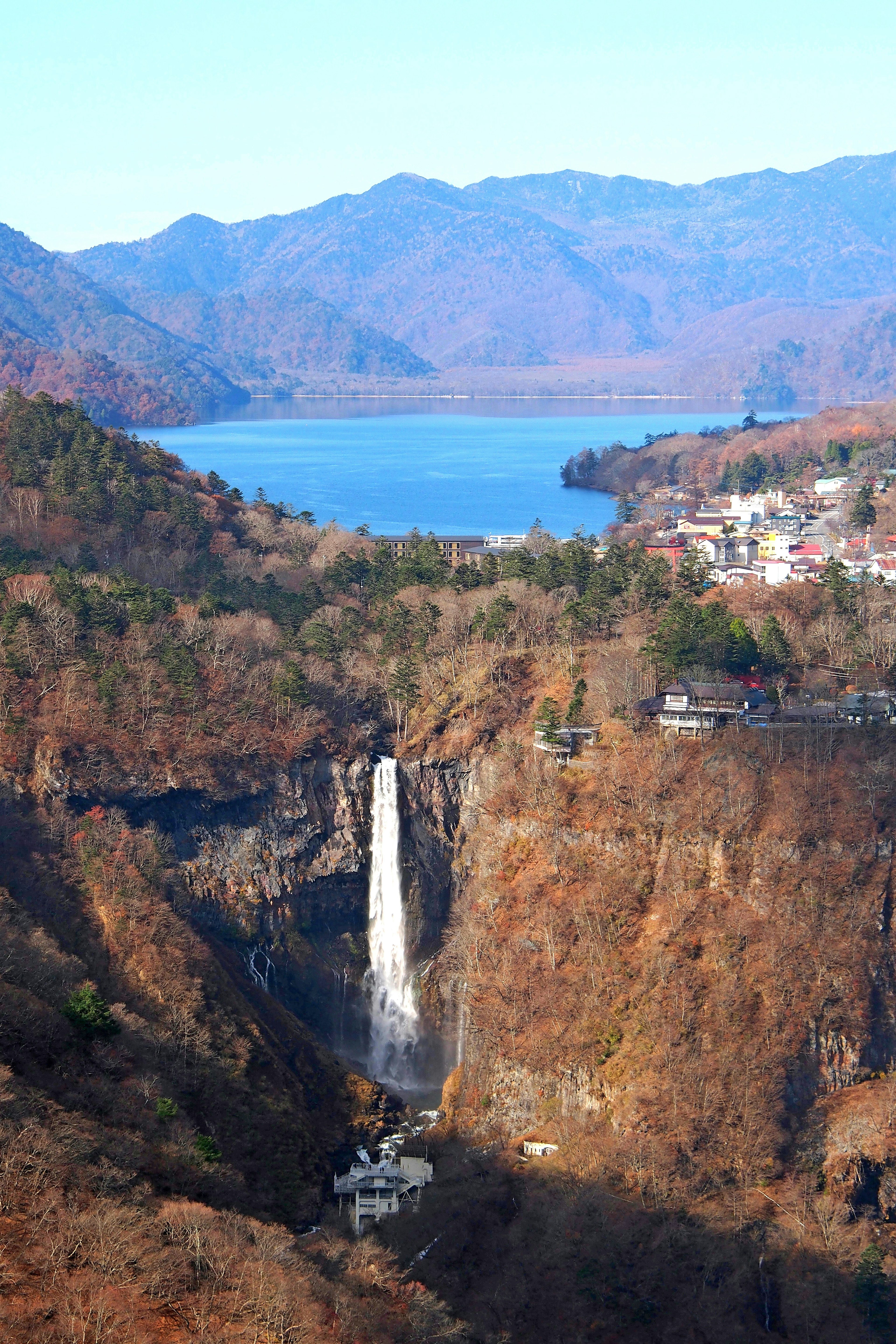 Vista panoramica di una cascata circondata da montagne e fogliame autunnale con un lago sullo sfondo