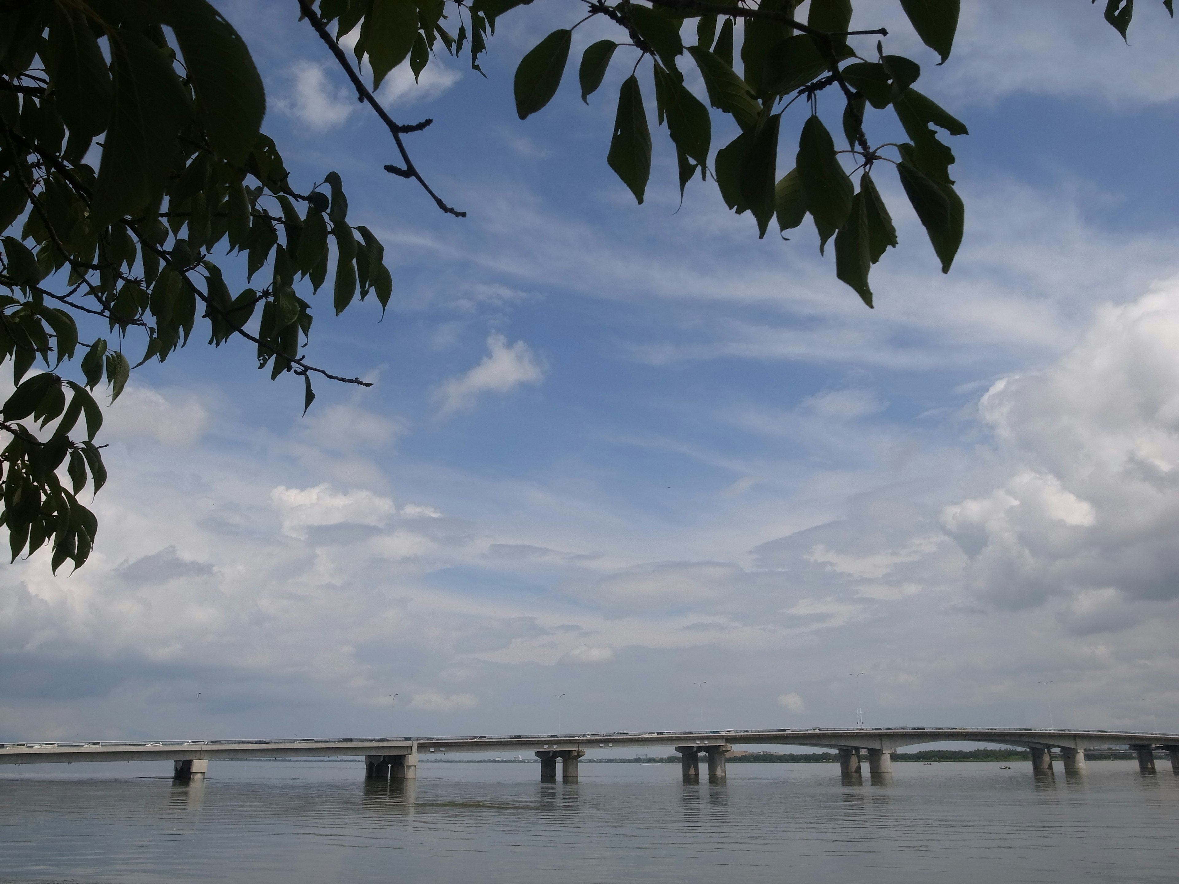 Un pont s'étendant au-dessus des eaux calmes sous un ciel bleu avec des nuages blancs