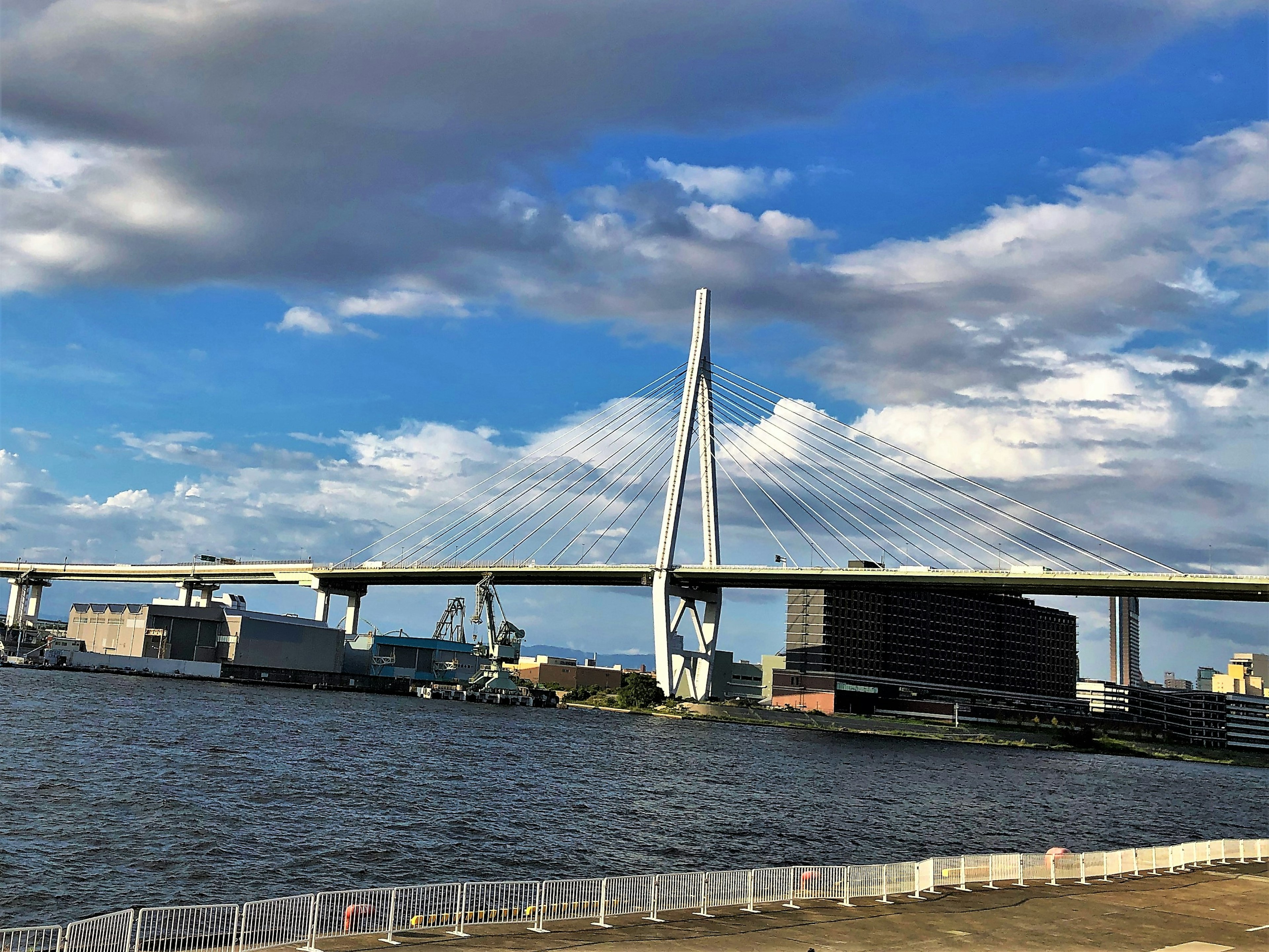 Jembatan besar yang melintasi sungai di bawah langit biru dengan awan