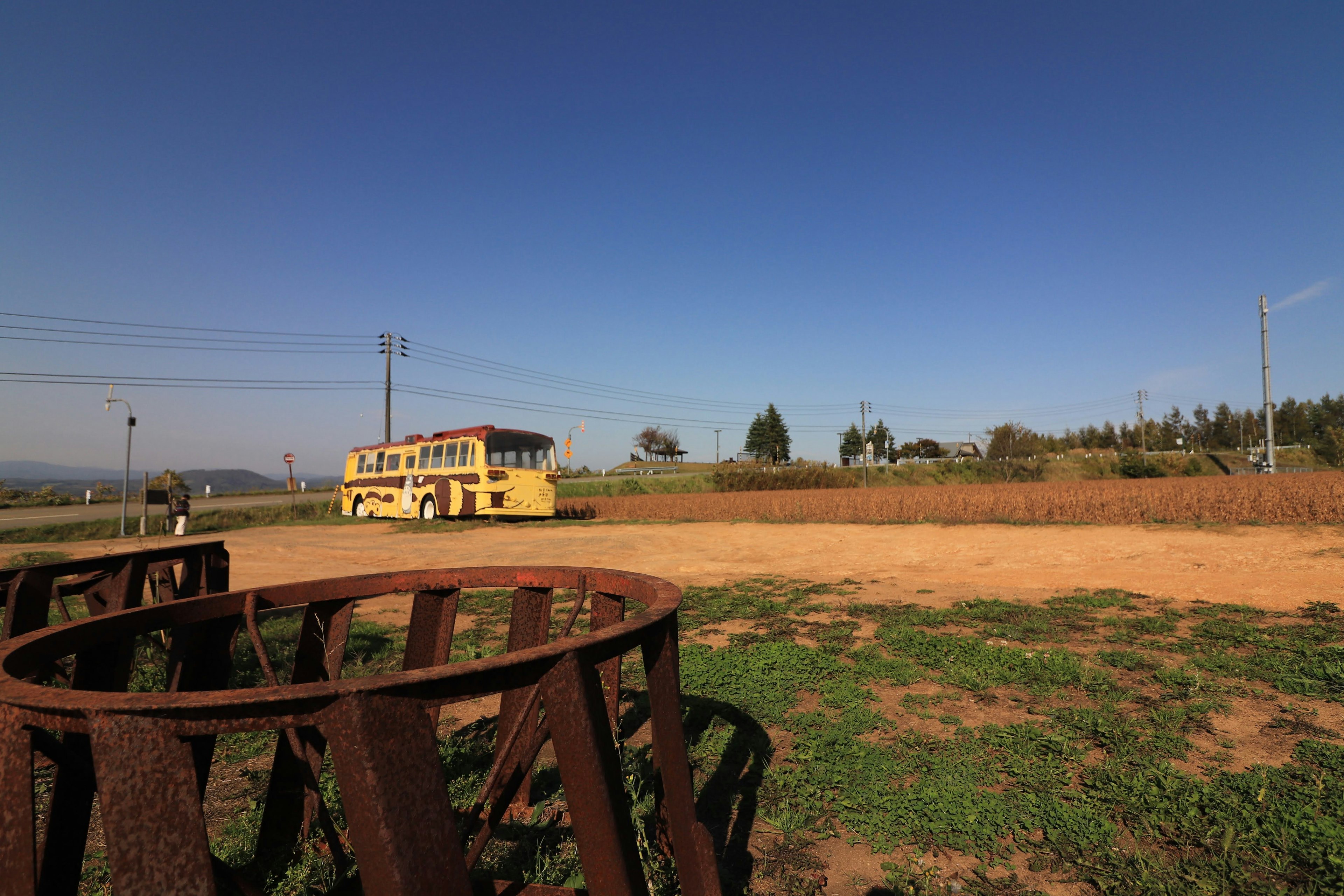 Gelber Bus unter einem weiten blauen Himmel rostige kreisförmige Struktur und grünes Grasfeld