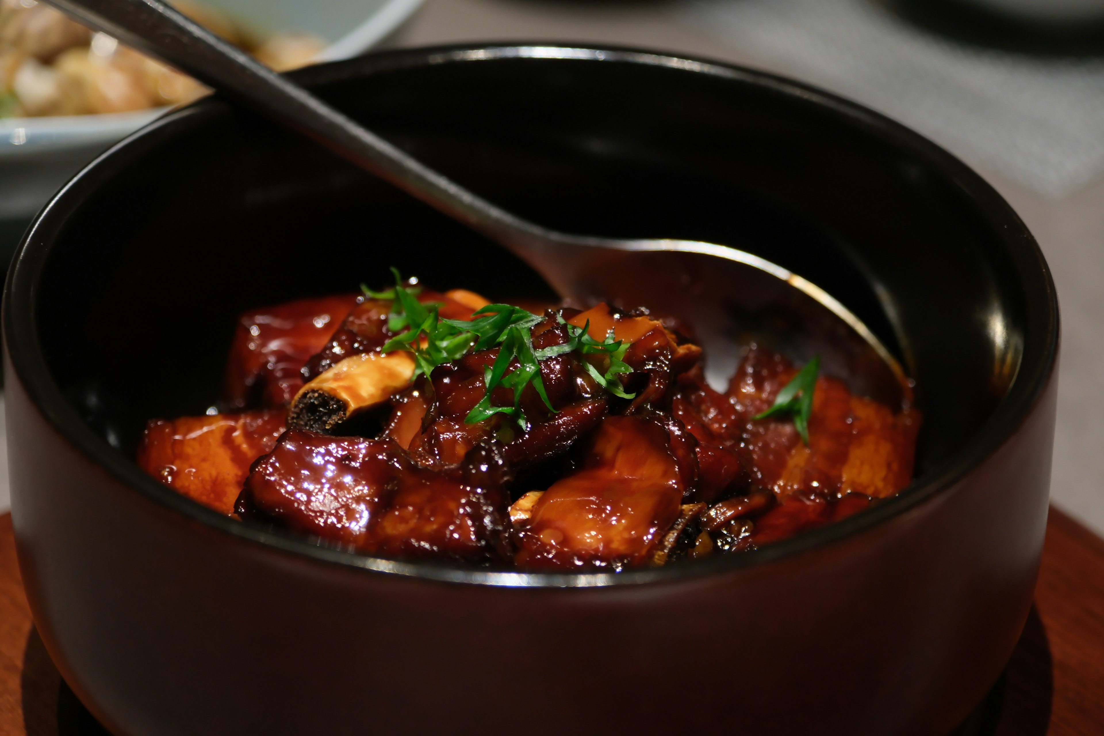 A dark bowl filled with a sweet and spicy dish garnished with herbs