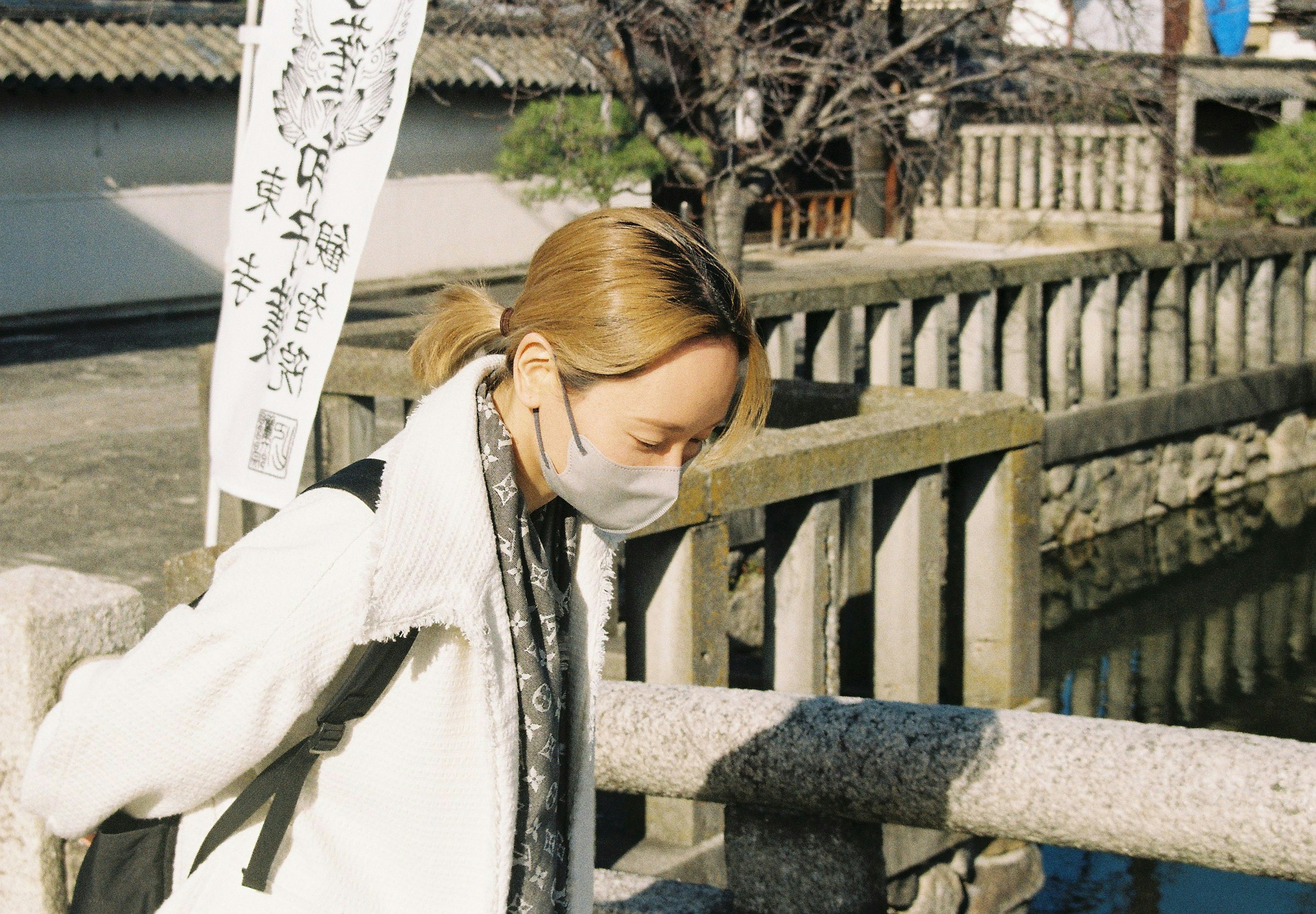 Femme masquée regardant vers le bas sur un pont portant une écharpe paysage japonais