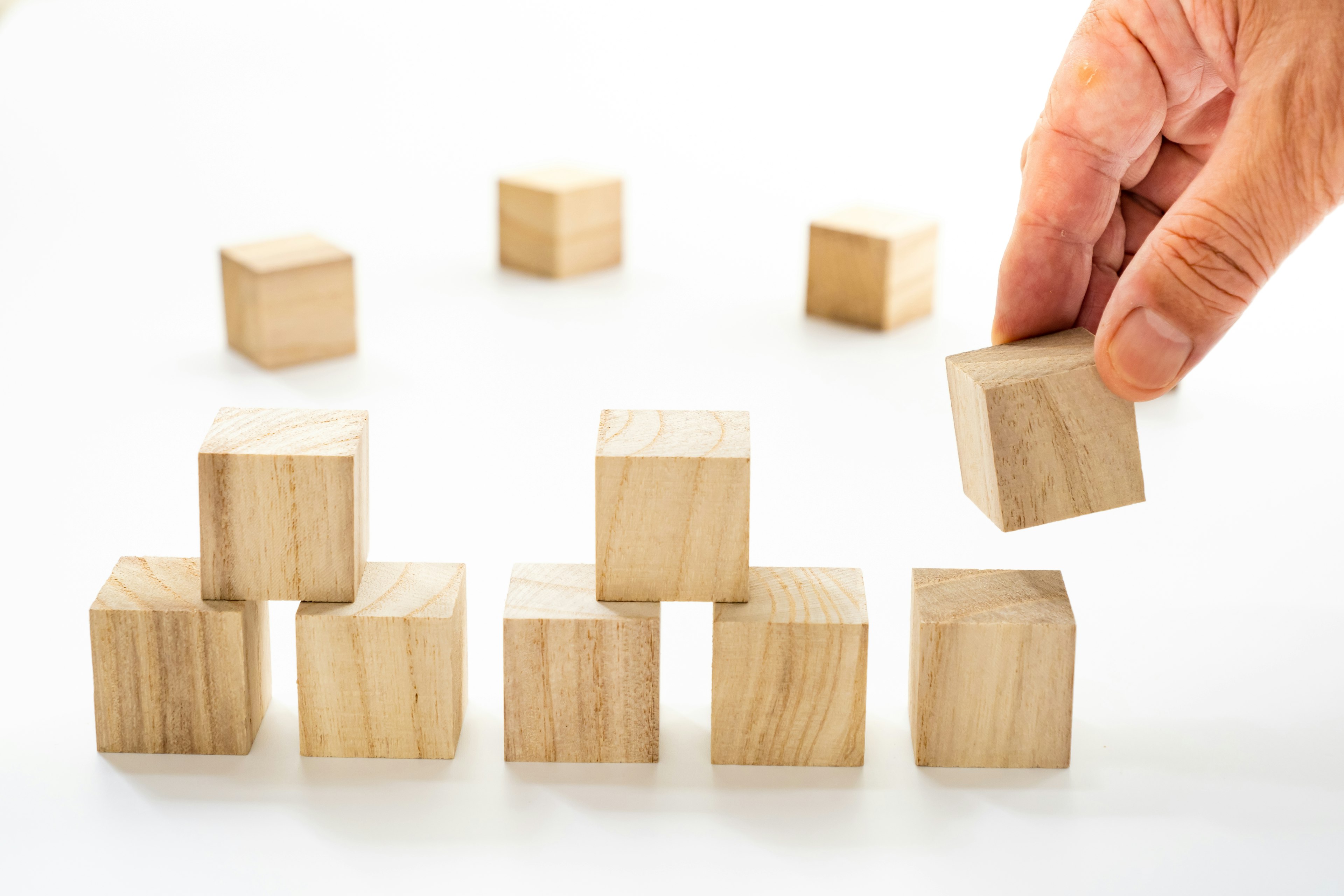 Eine Hand platziert einen Holzblock zwischen angeordneten Holzblöcken