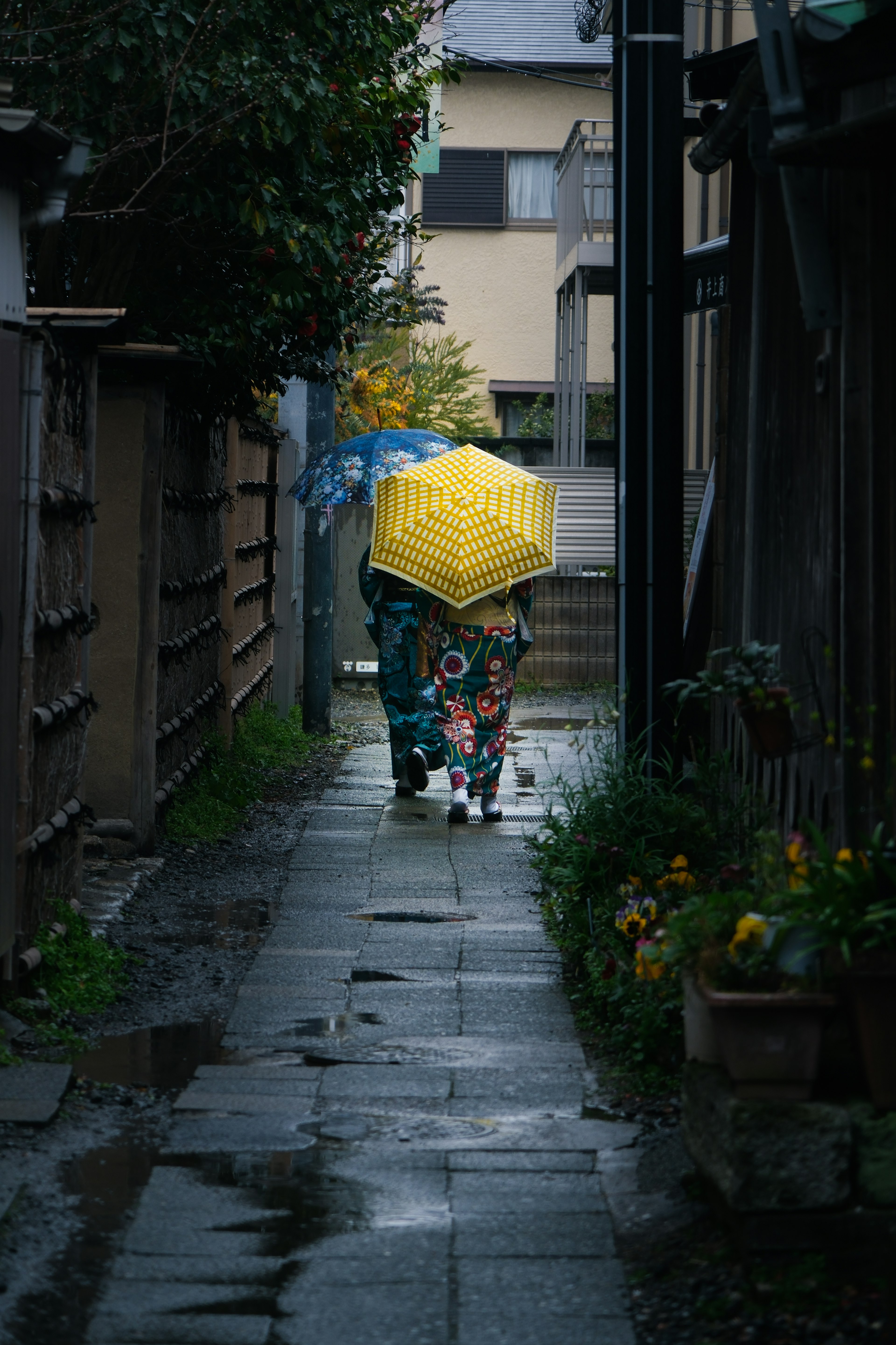 雨の中で黄色い傘をさした人が歩いている狭い路地の風景