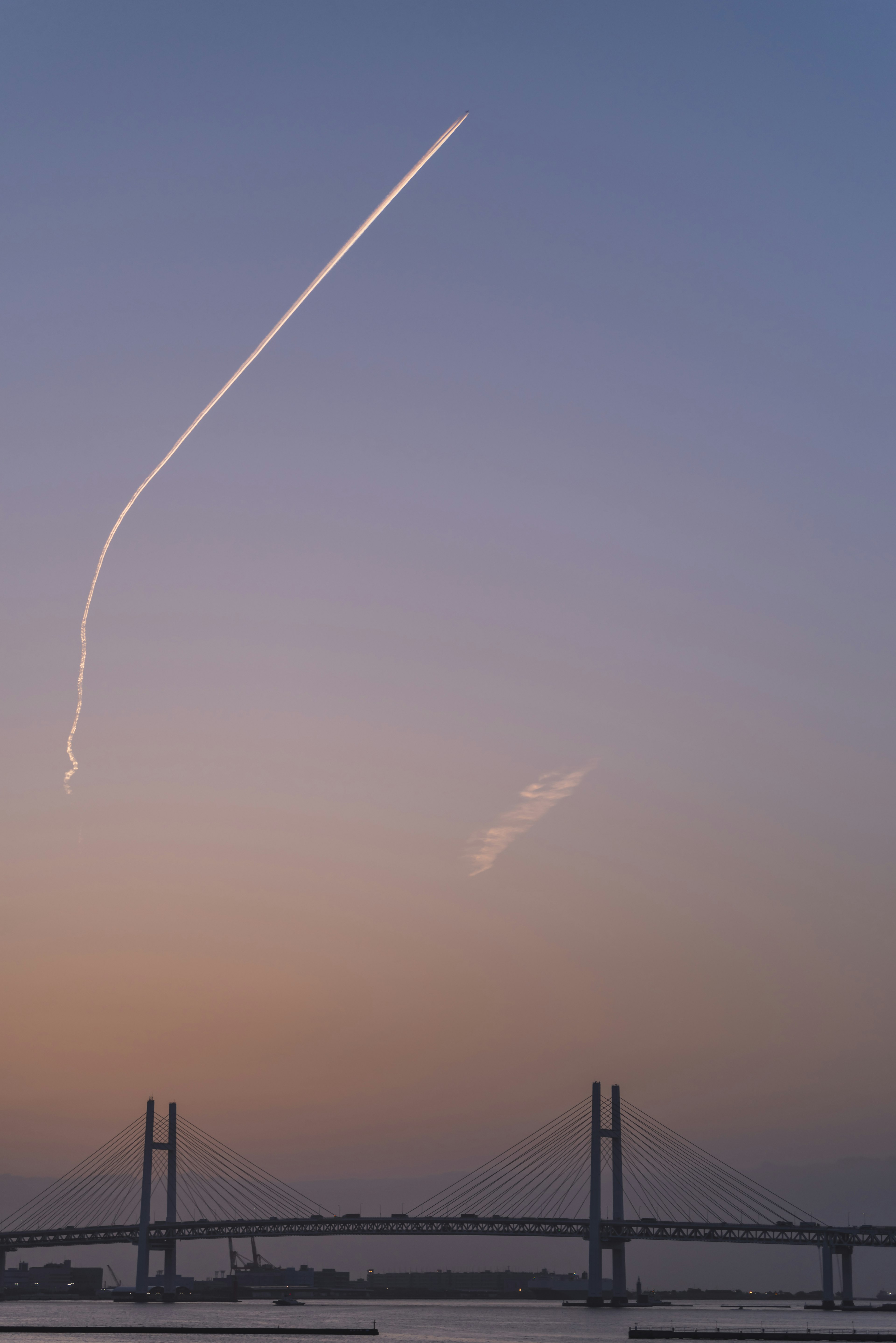 夕焼けの空に飛行機雲が描く美しい軌跡と橋のシルエット