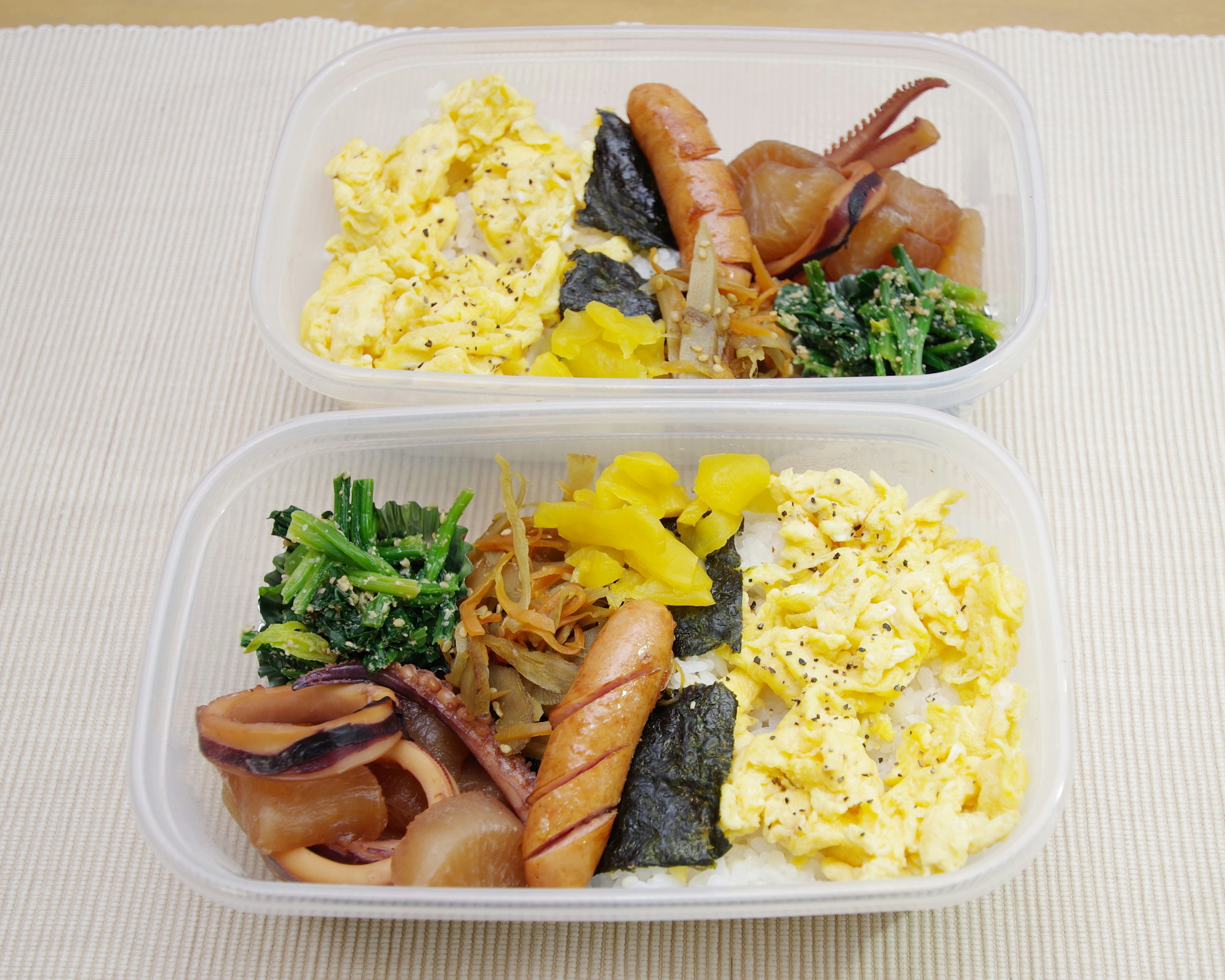 Two-tier bento box featuring scrambled eggs, sausages, squid, seaweed, spinach, and pickles