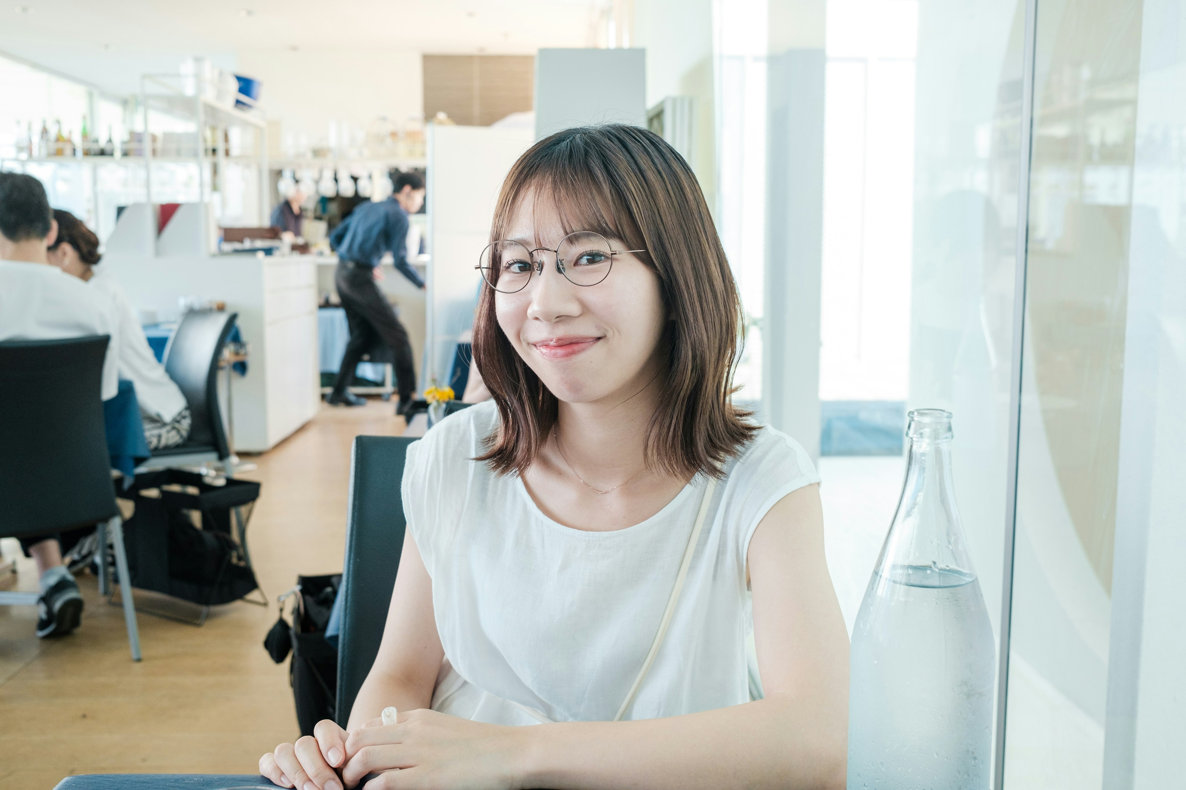 Portrait d'une femme souriante dans un café portant une chemise blanche avec des gens en arrière-plan