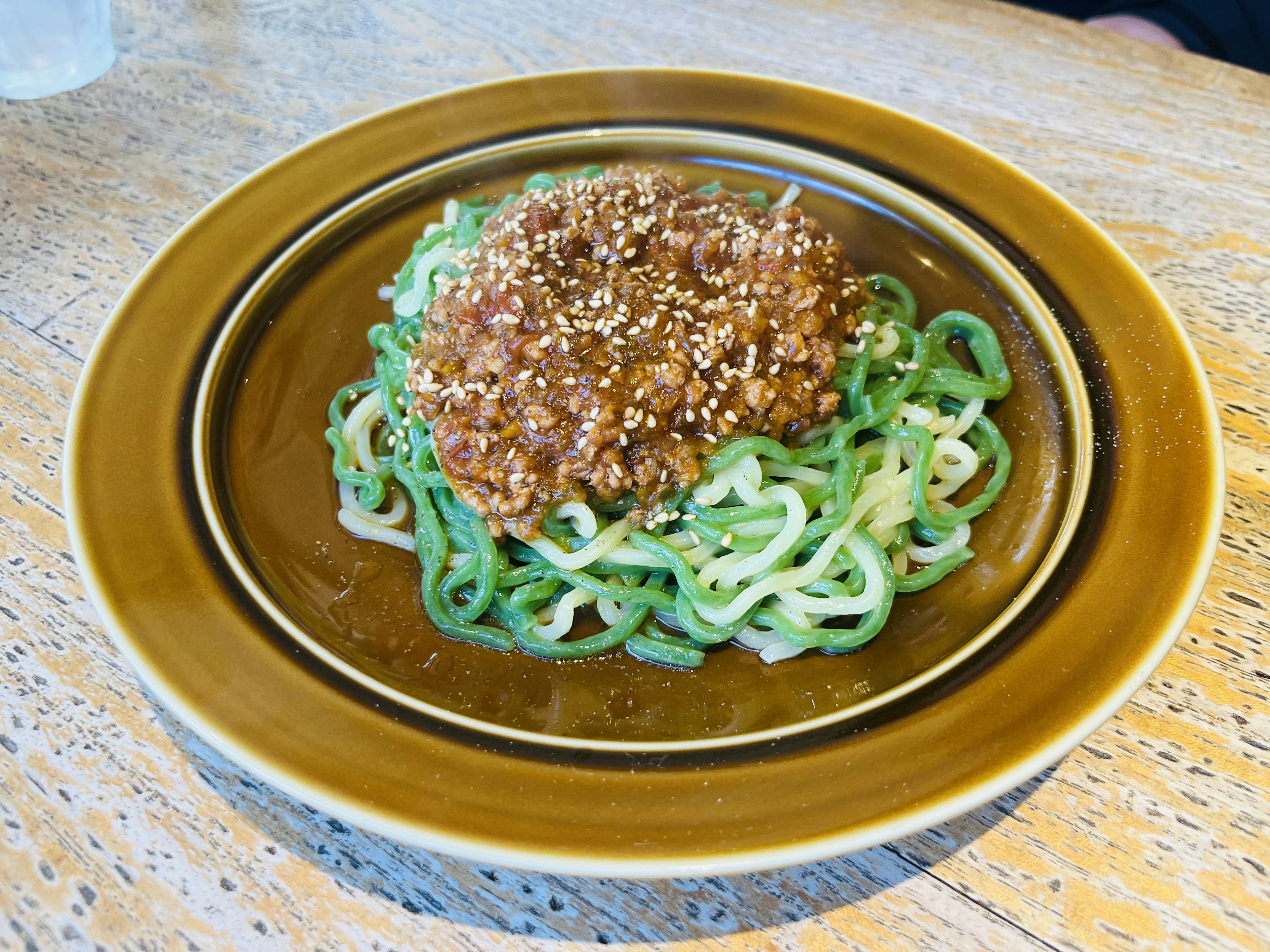 Plate of green noodles topped with meat sauce and sesame seeds