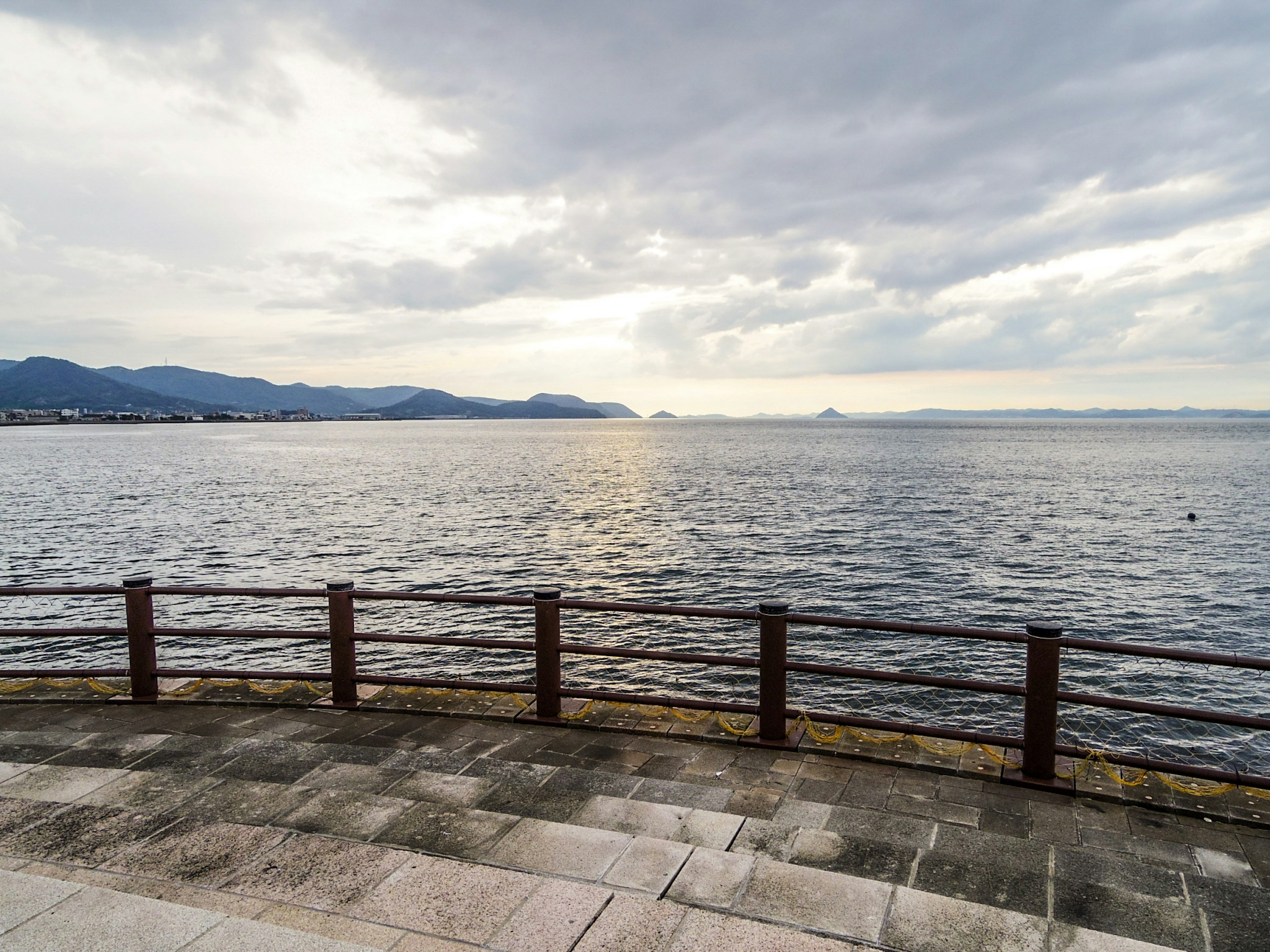 平靜的海洋和多雲的天空景觀，岸邊有鐵欄杆