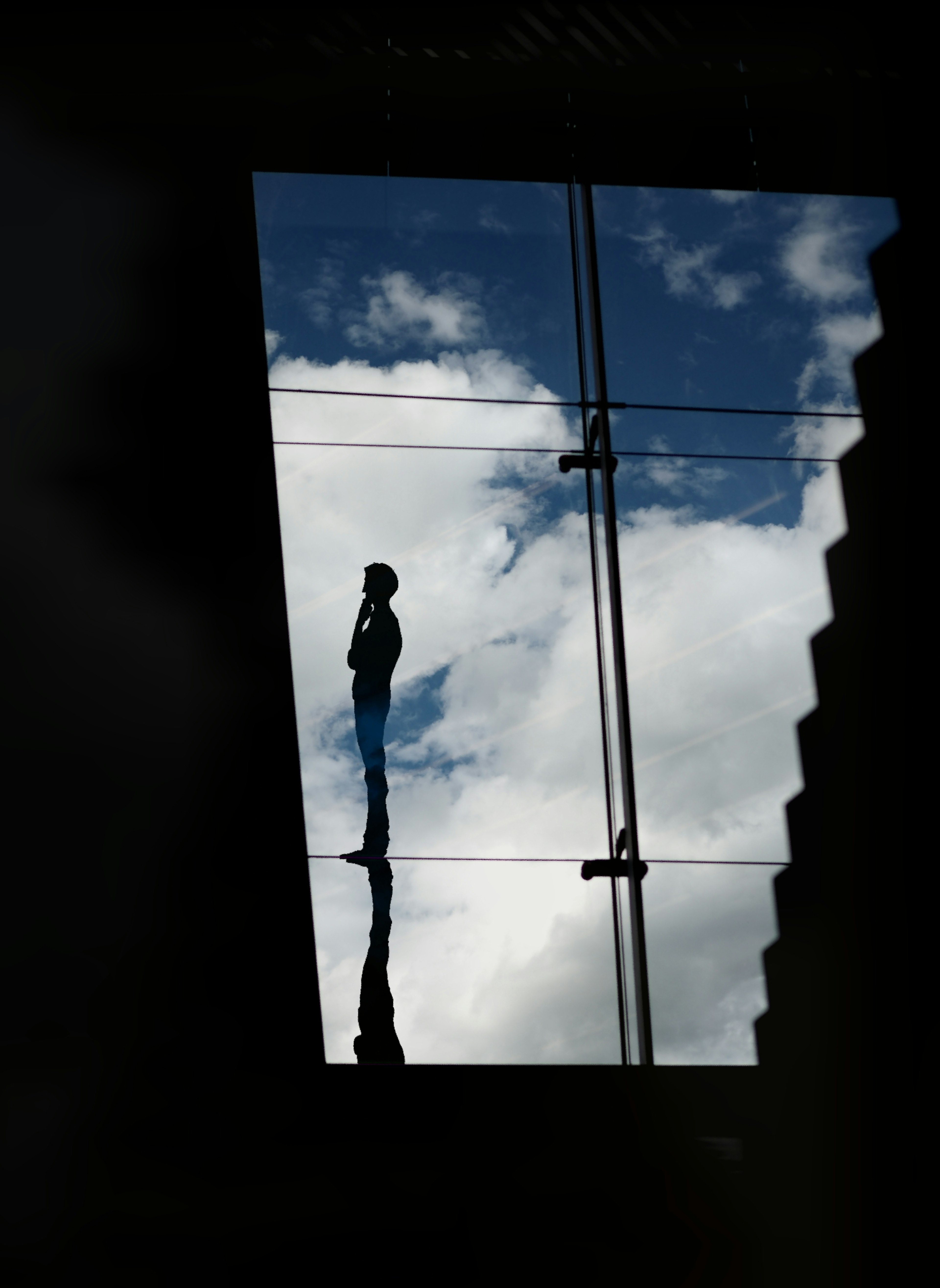 Silhouette of a person reflected on a glass window with clouds