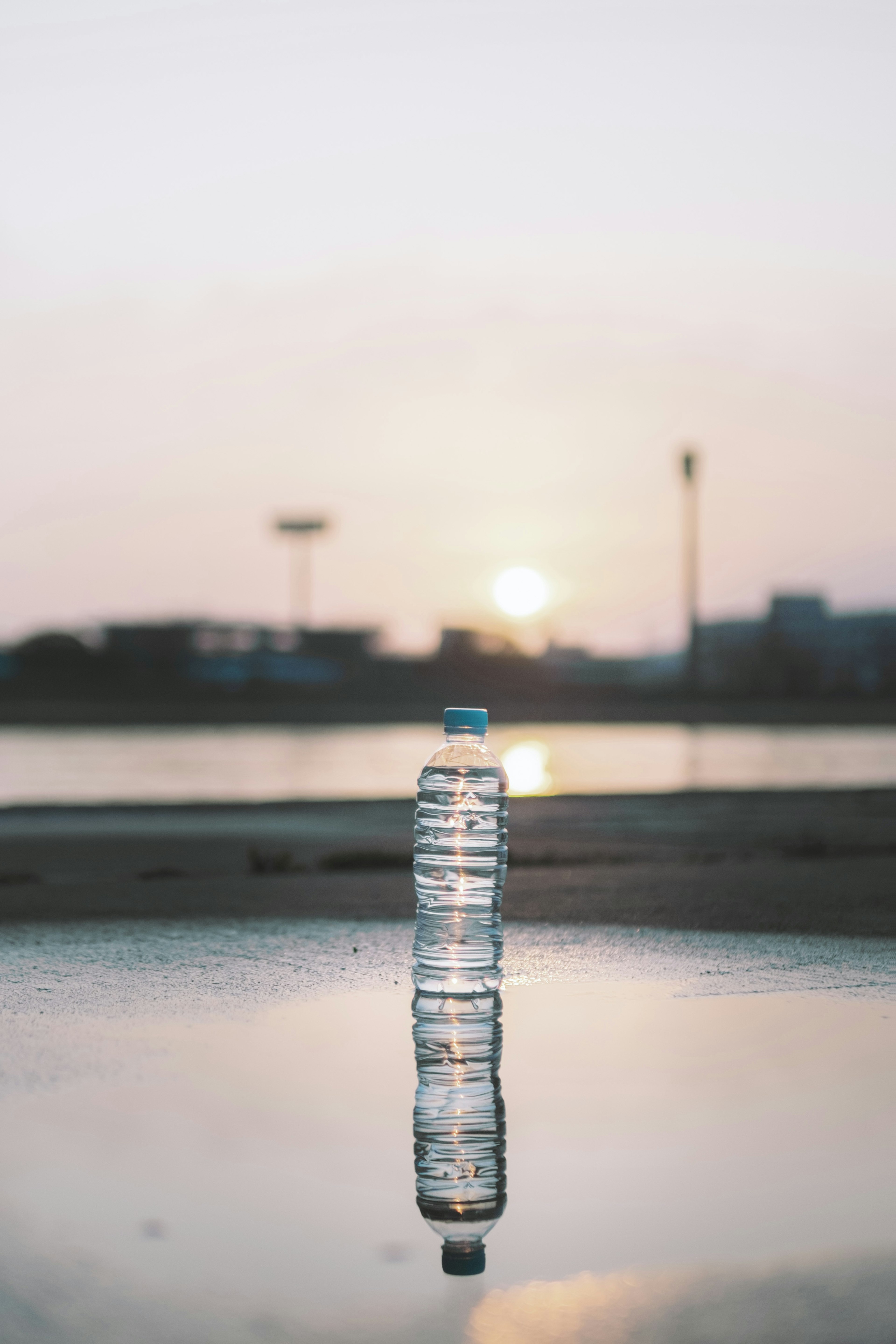 Una botella de agua de plástico transparente de pie en un charco reflectante al amanecer