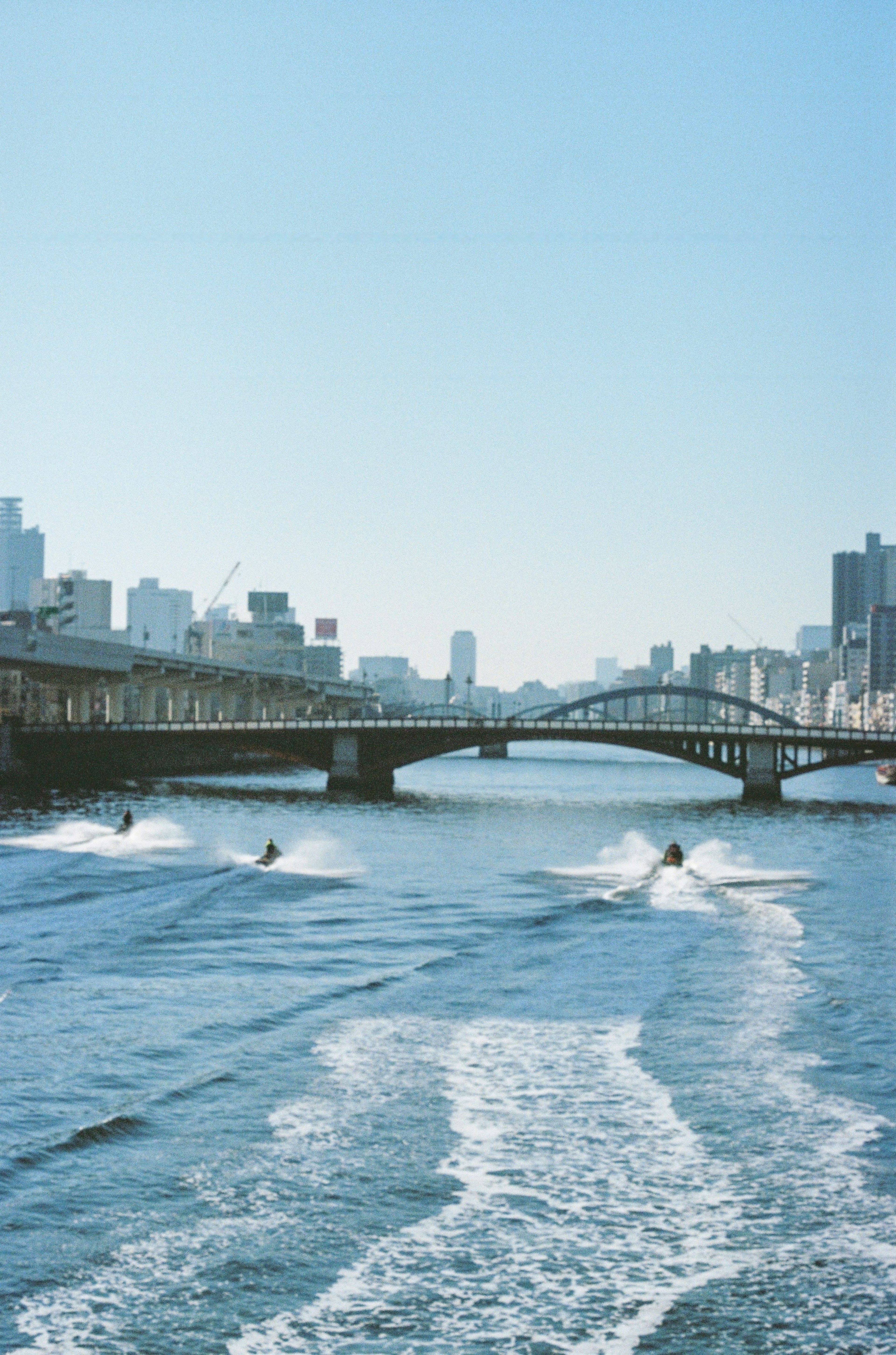 青い空と都市の背景を持つ川の風景 ボートが水面を滑る様子 橋が遠くに見える