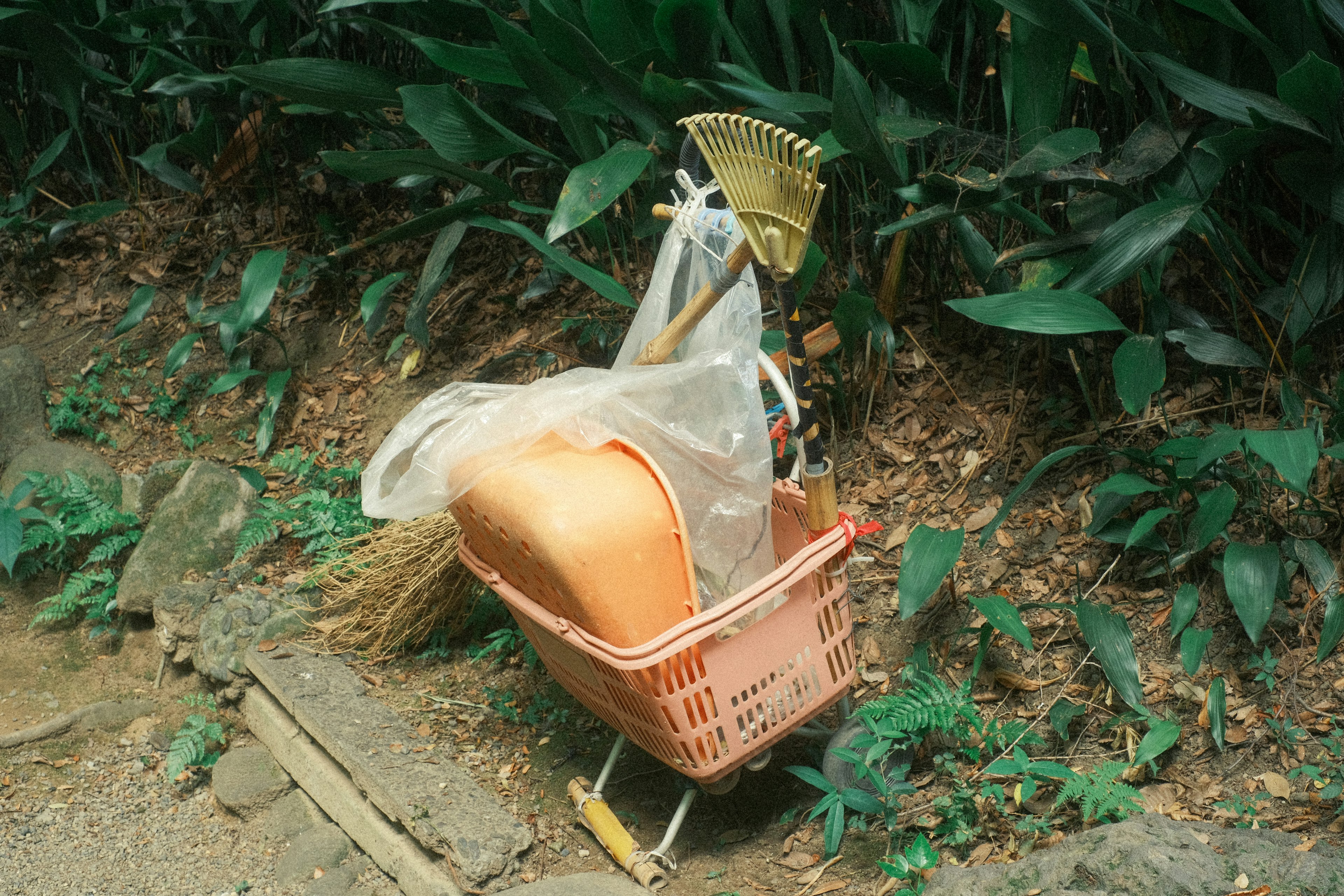 Una cesta de jardinería al borde de la carretera que contiene una maceta naranja y una escoba