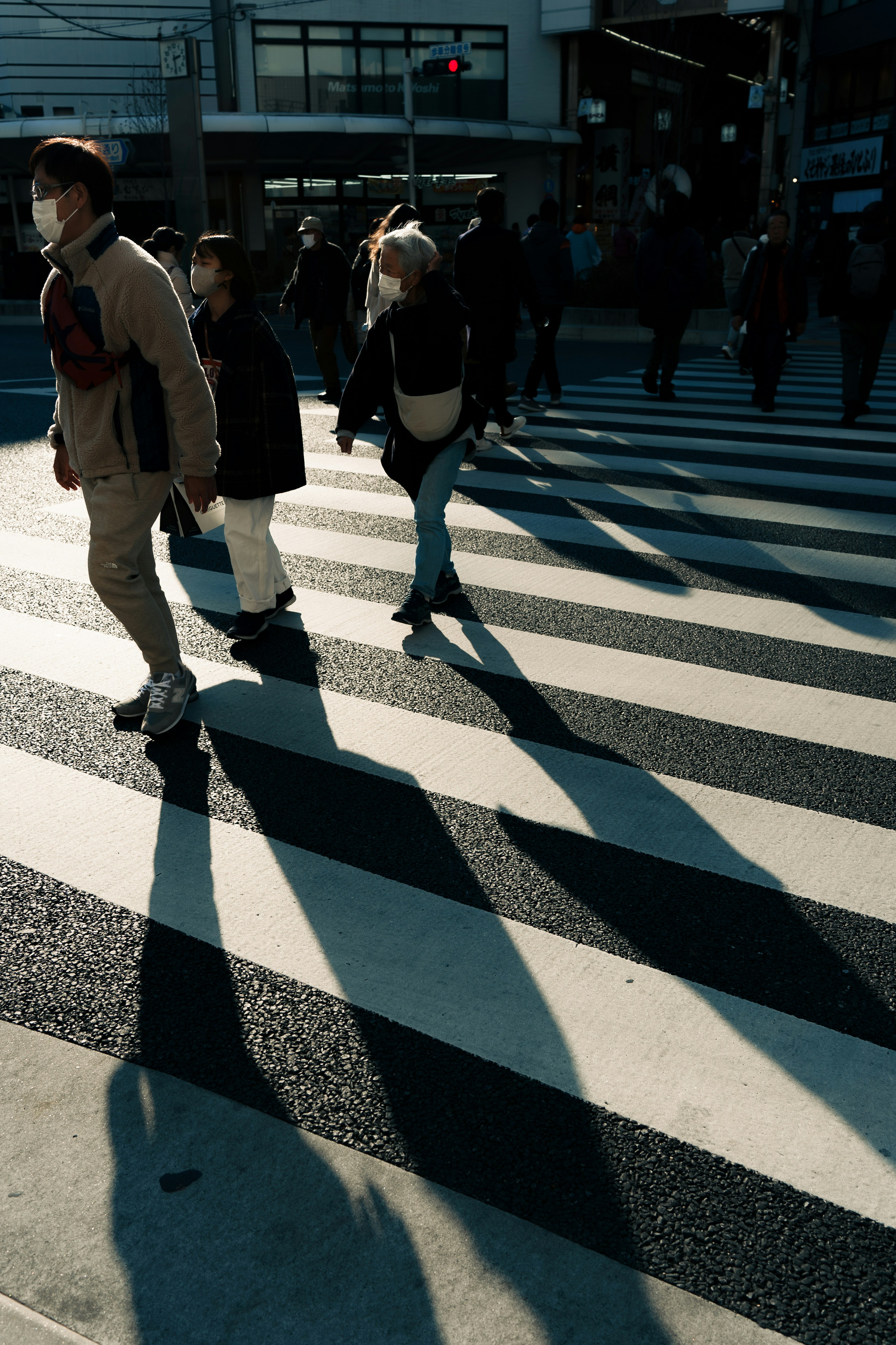 People crossing a pedestrian crosswalk with long shadows cast by sunlight