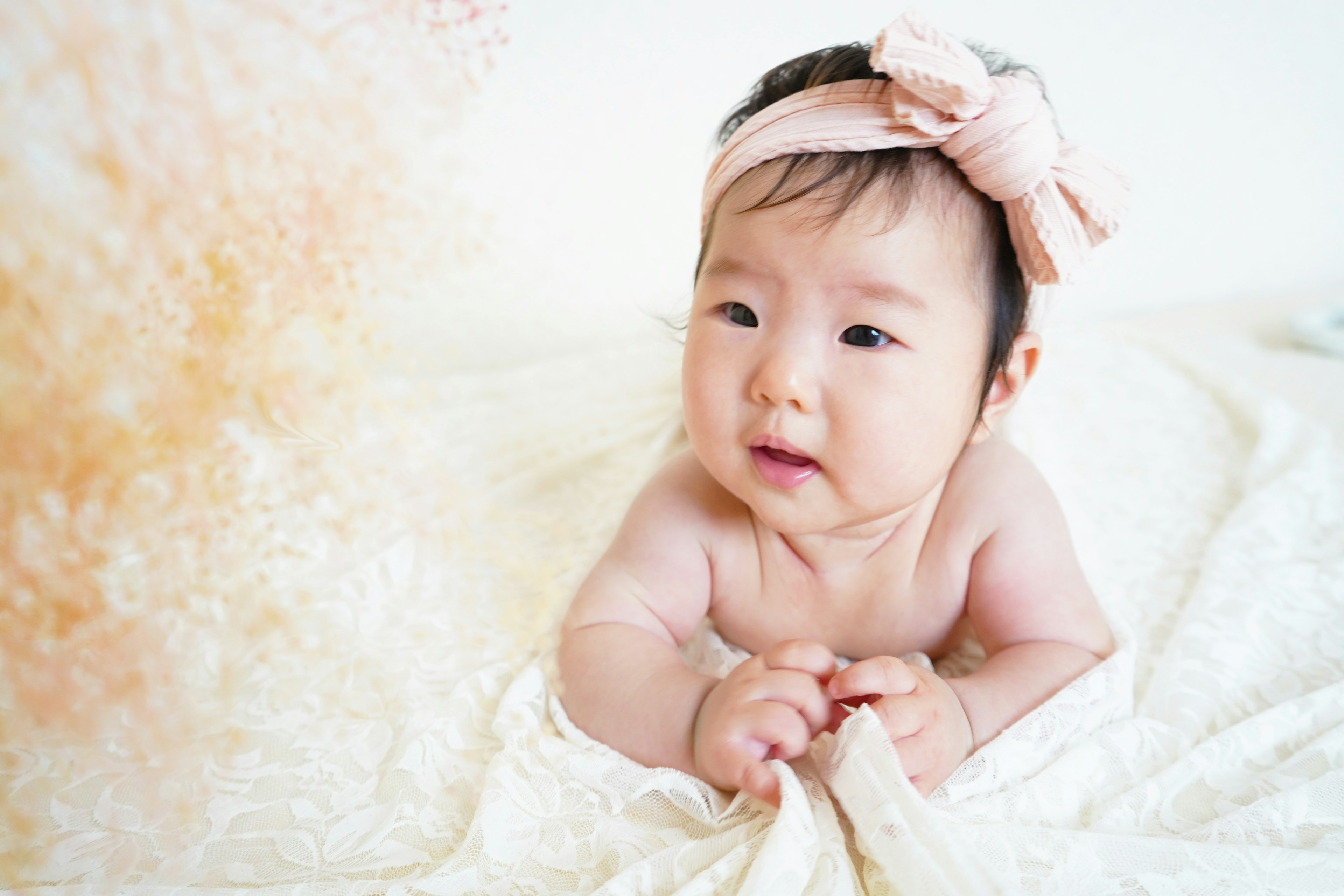 Baby on a white blanket with a pink bow on the head against a beige background