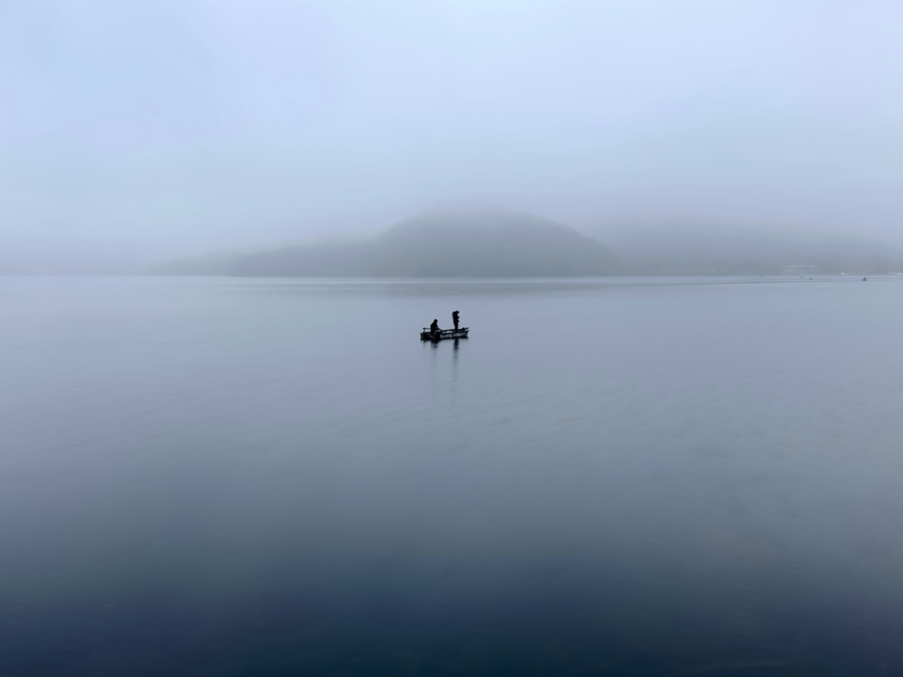 Two fishermen in a boat on a calm lake surrounded by fog