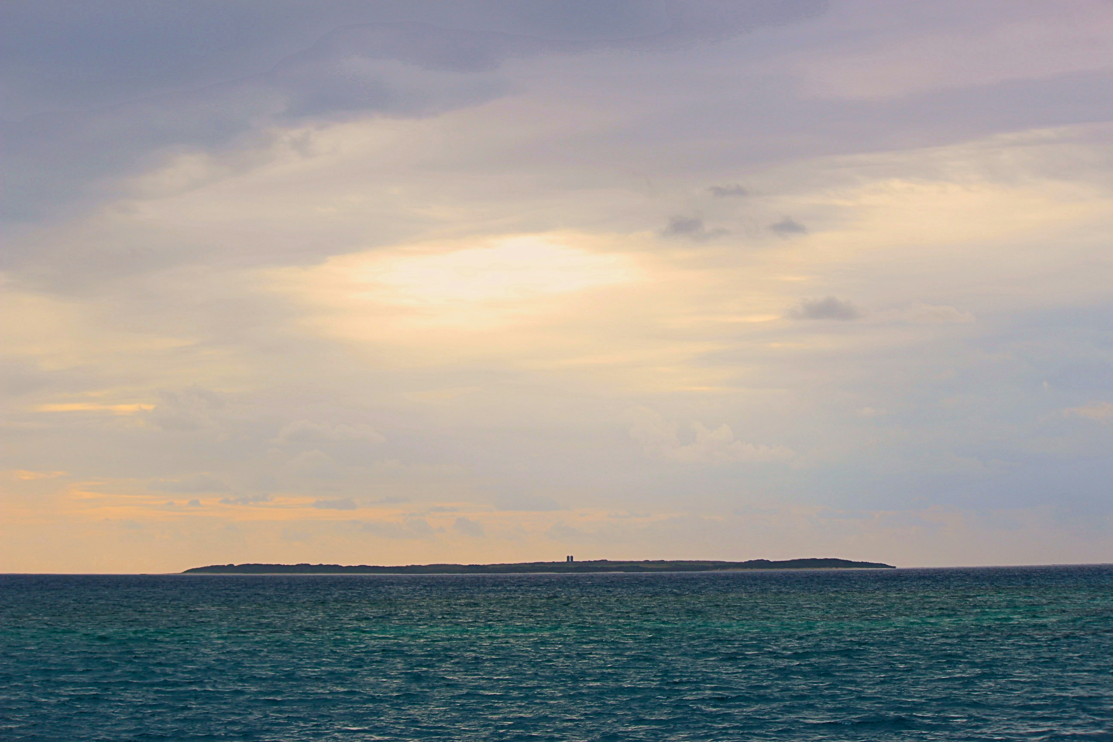 海と空が広がる風景 薄曇りの空に夕焼けの光が差し込む