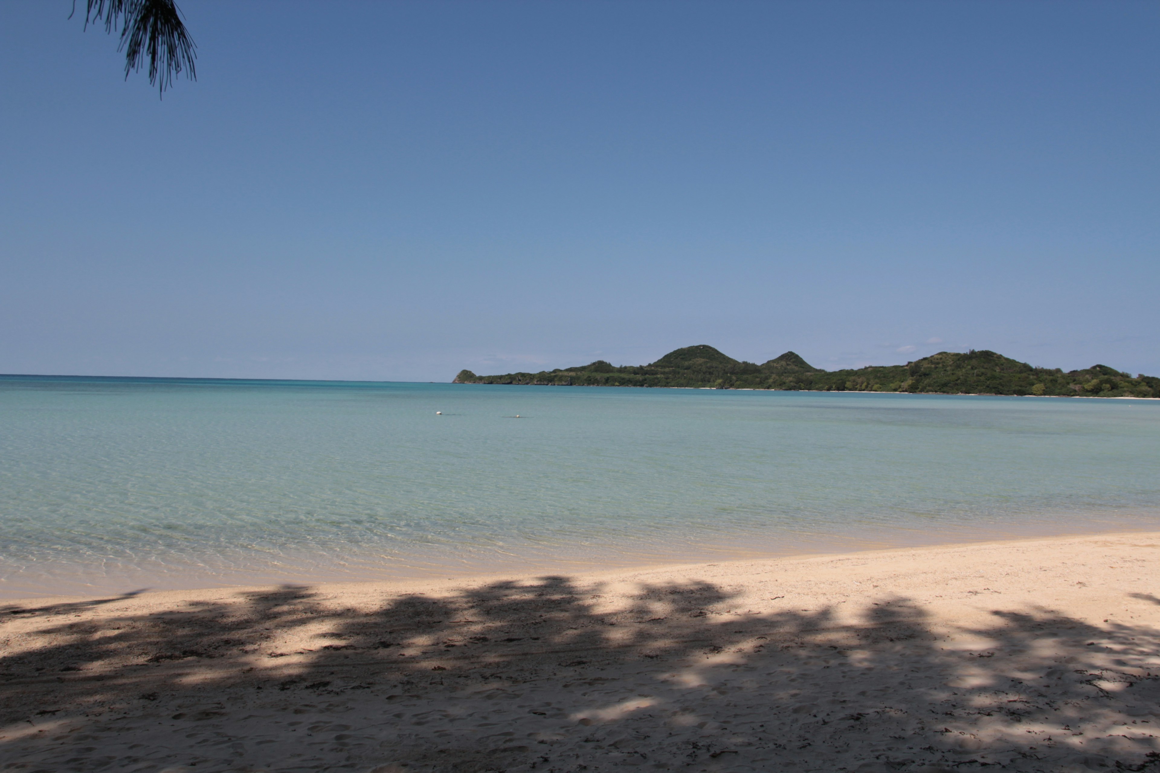 Pemandangan pantai tenang dengan air biru dan pulau-pulau di kejauhan