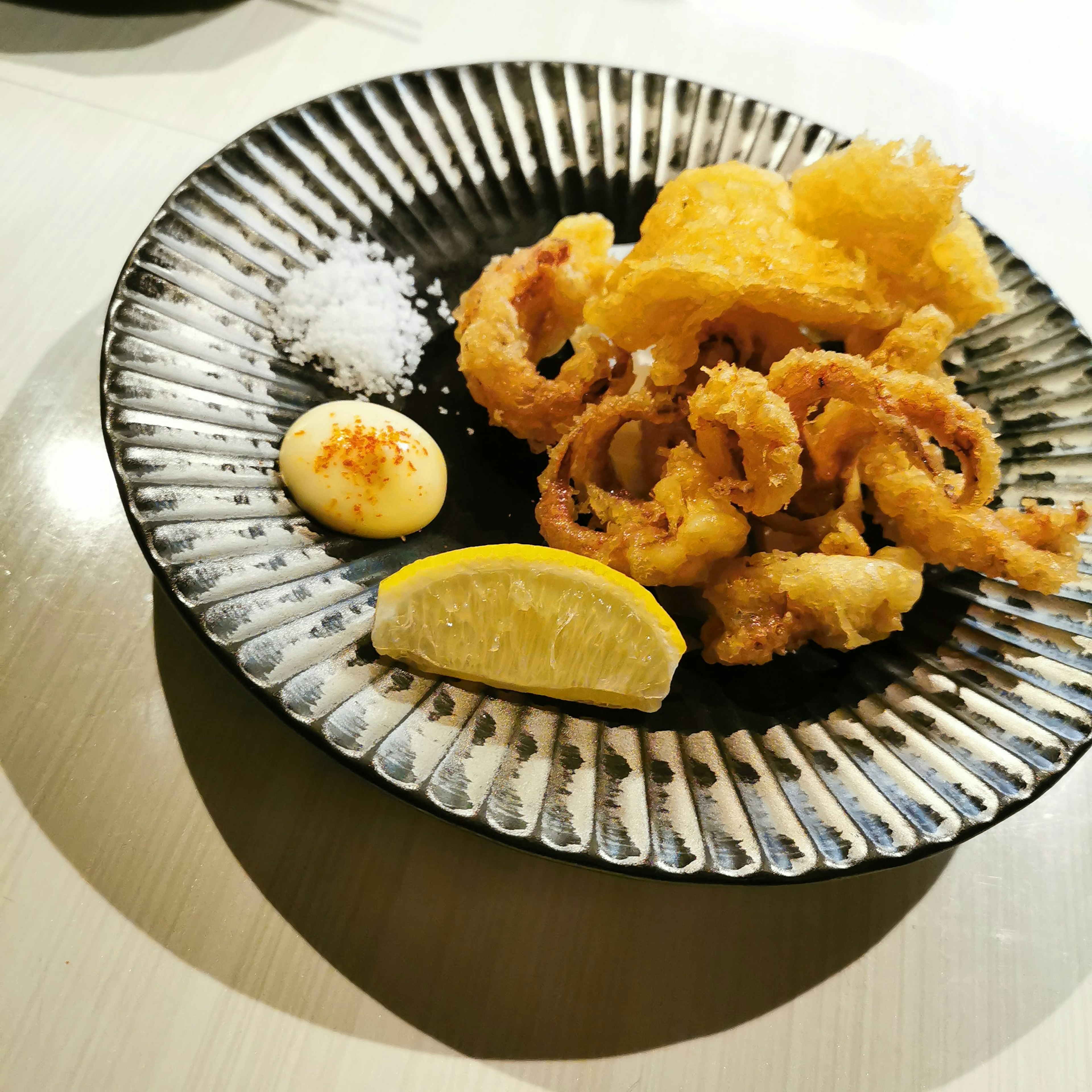 Calamars frits servis sur une assiette noire avec une tranche de citron et du sel