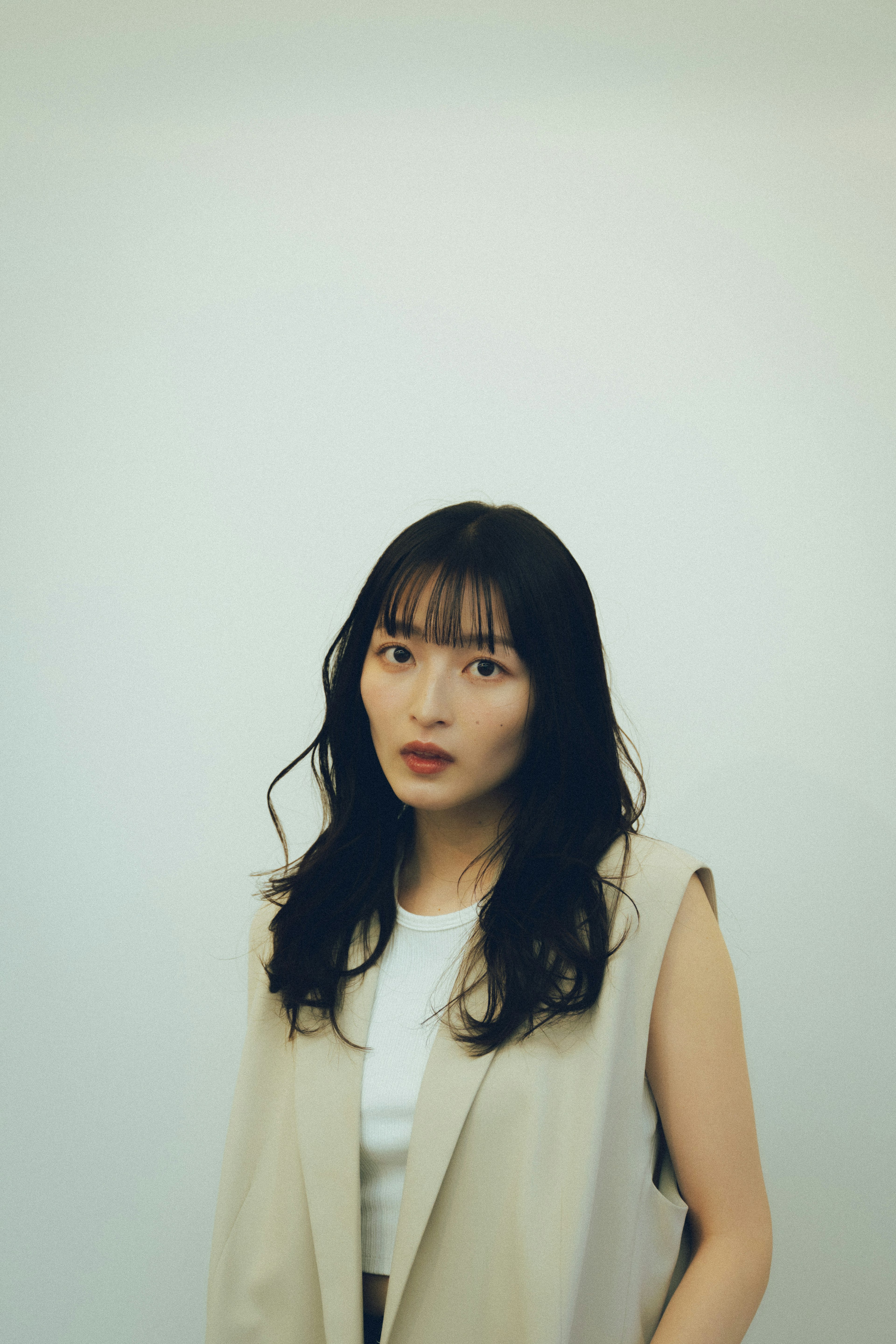 Portrait of a woman standing against a white background with short bangs and long wavy hair