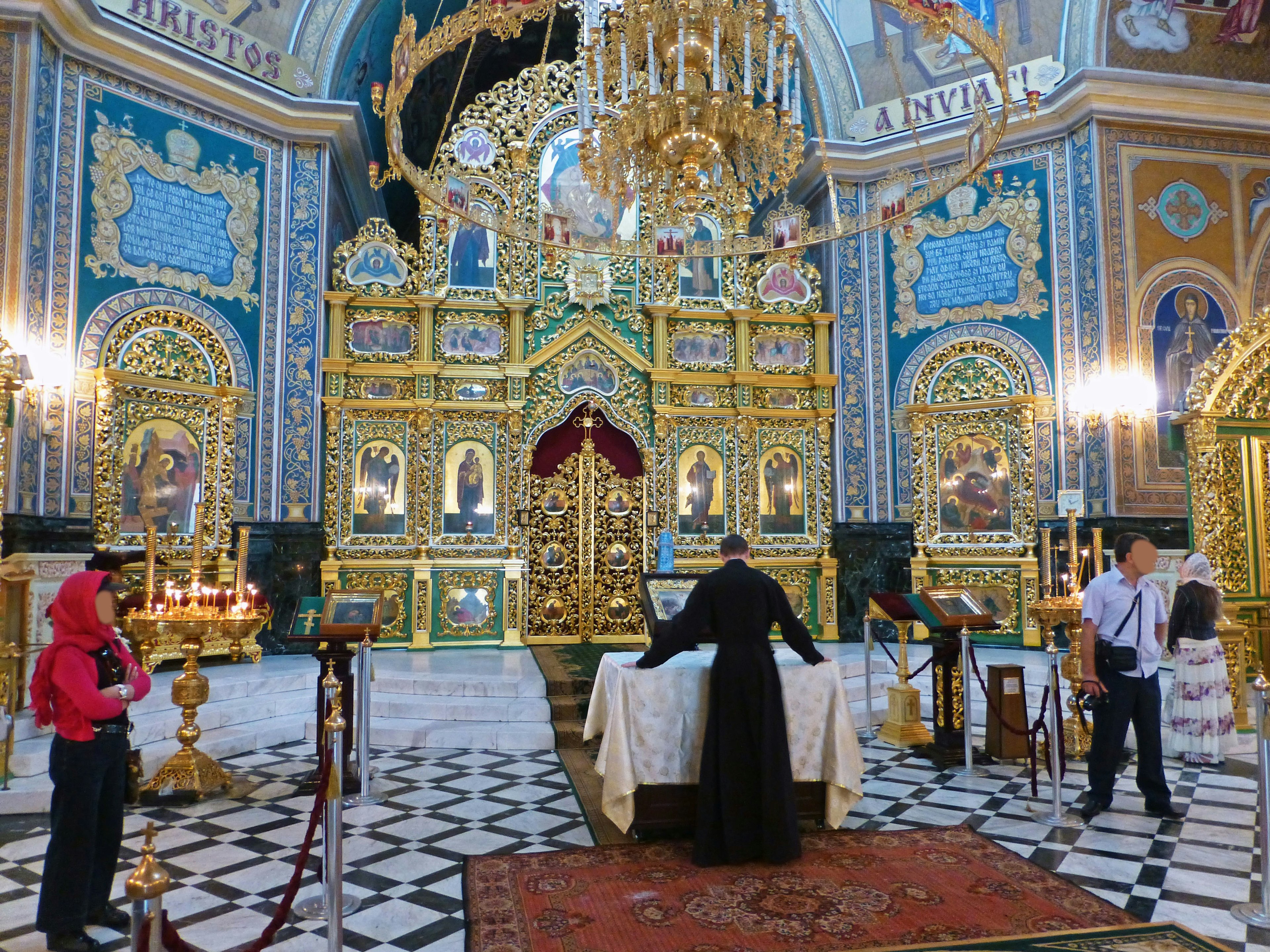 Innenraum einer verzierten Kirche mit einem Priester am Altar und Besuchern