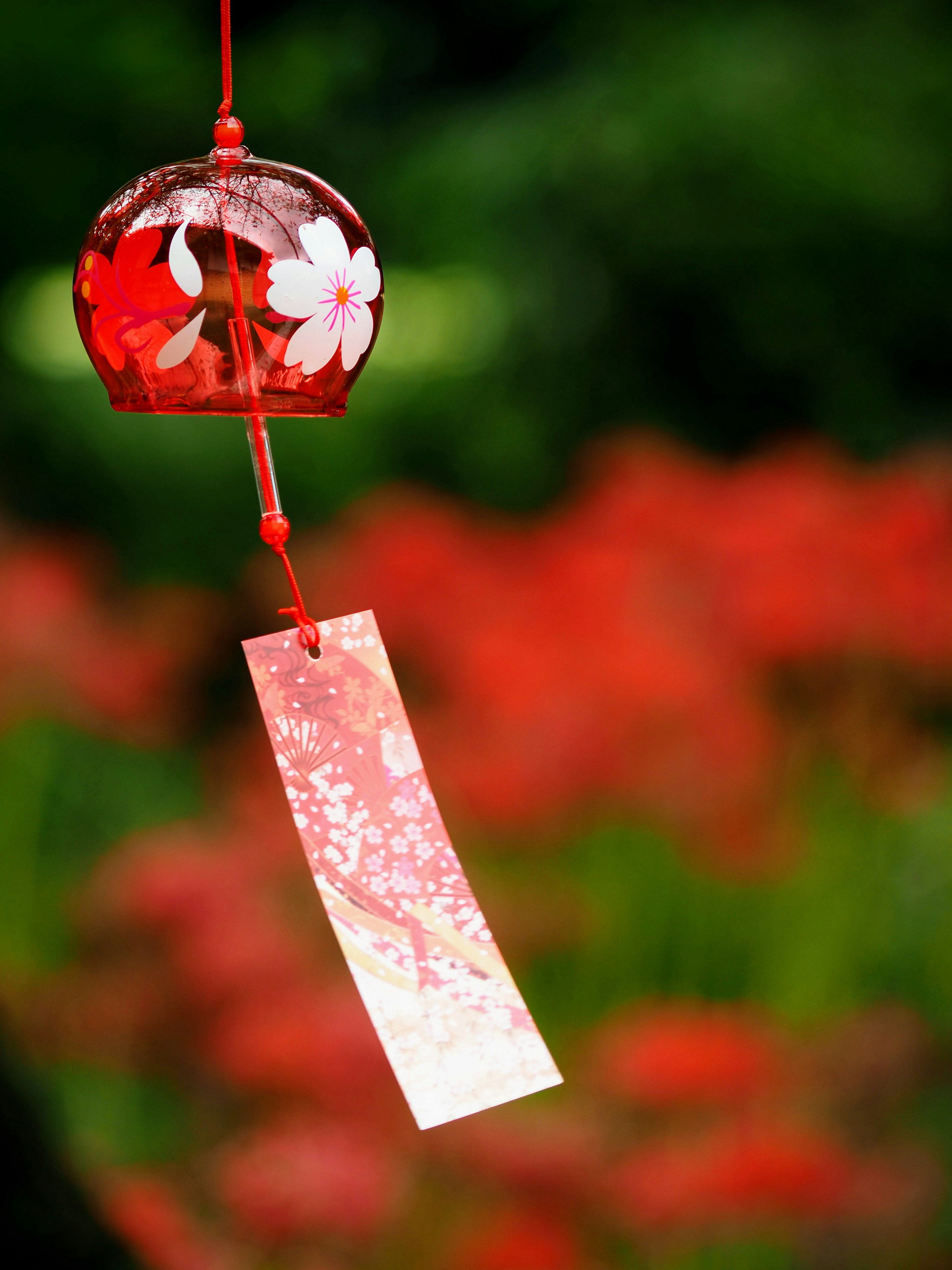 Un carillon rouge avec des motifs floraux et une bande de papier suspendue dans un jardin vibrant