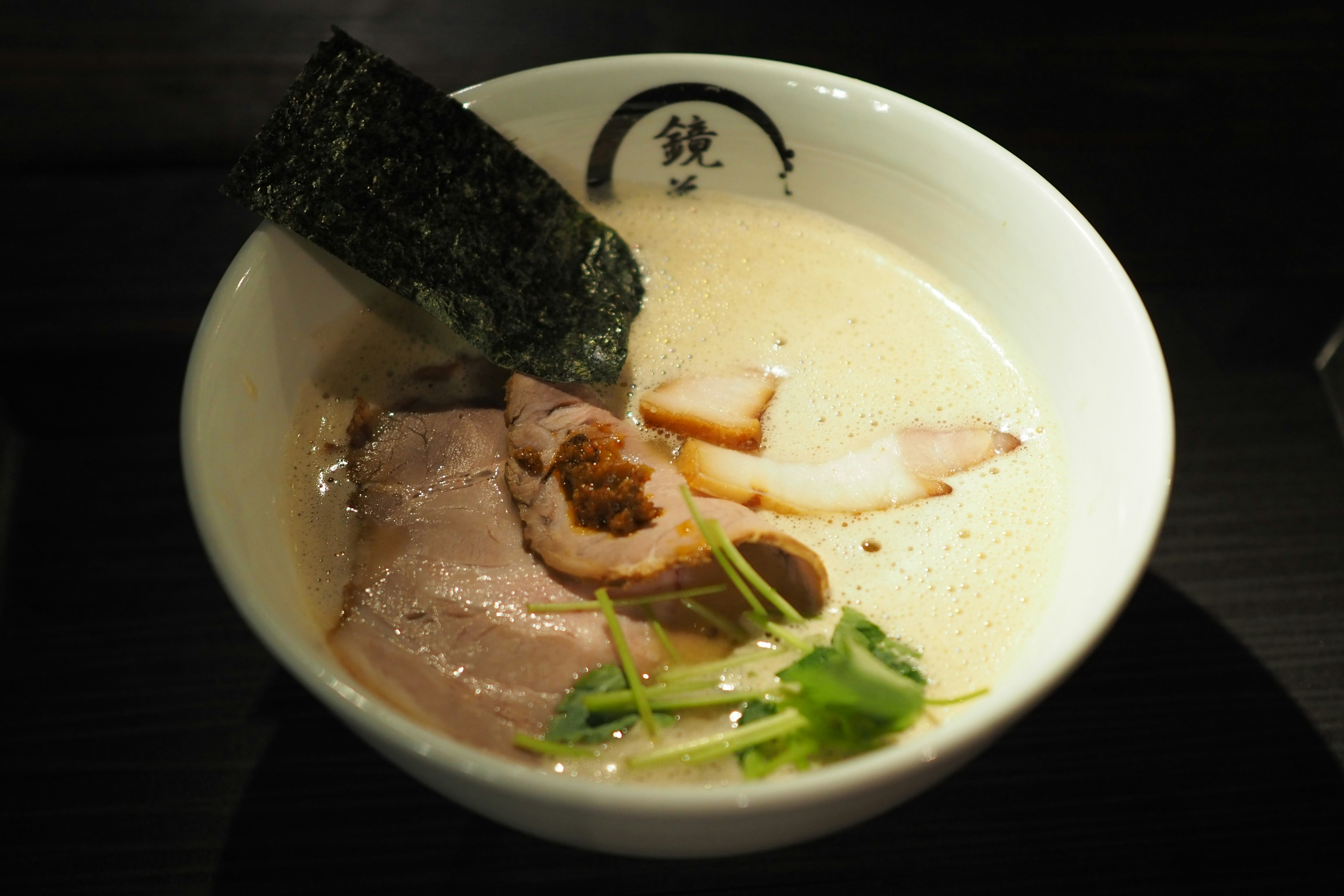 Ciotola di zuppa ramen cremosa guarnita con fette di chashu e alga nori