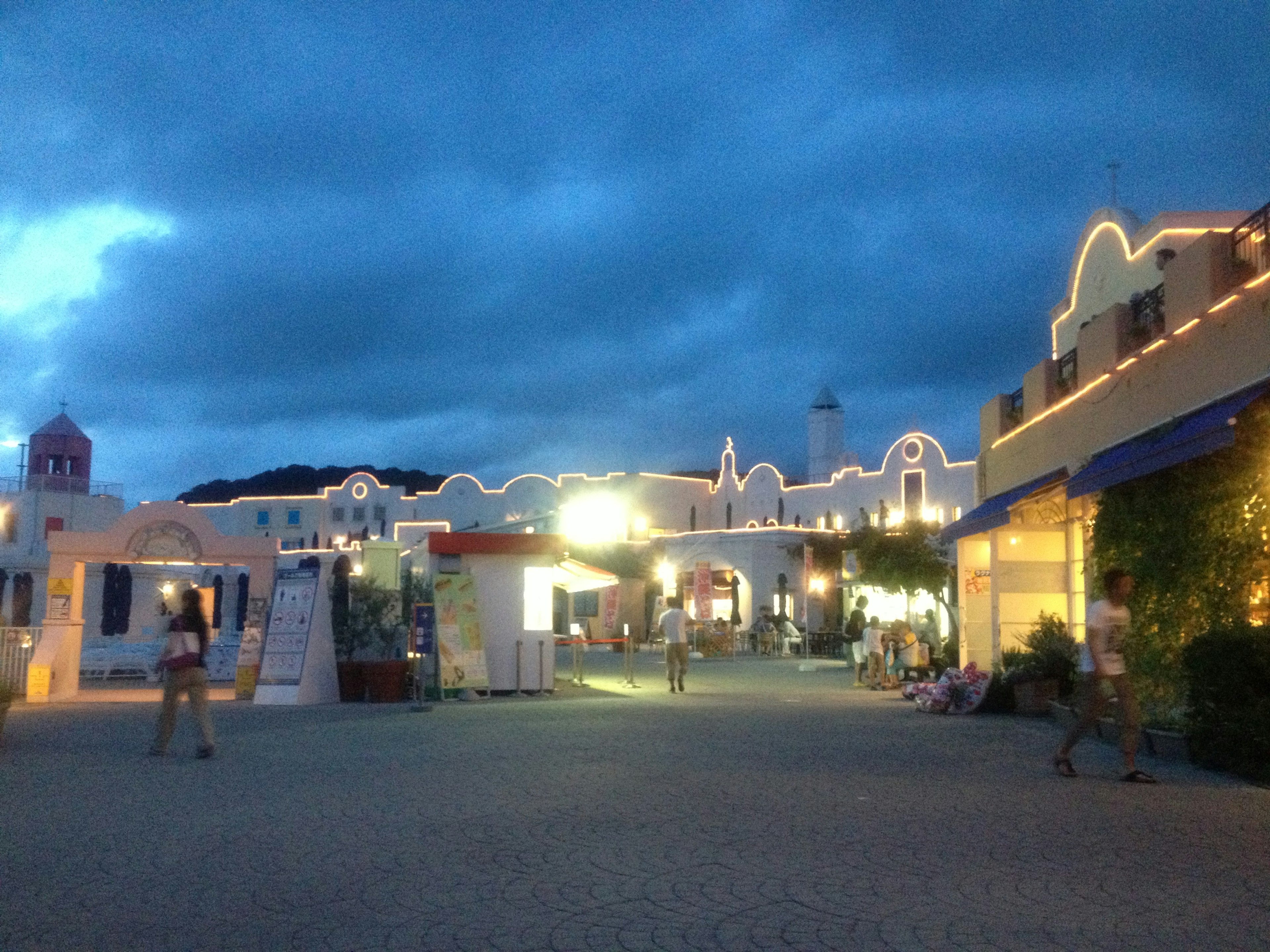 Street scene with illuminated buildings under a blue sky and people walking