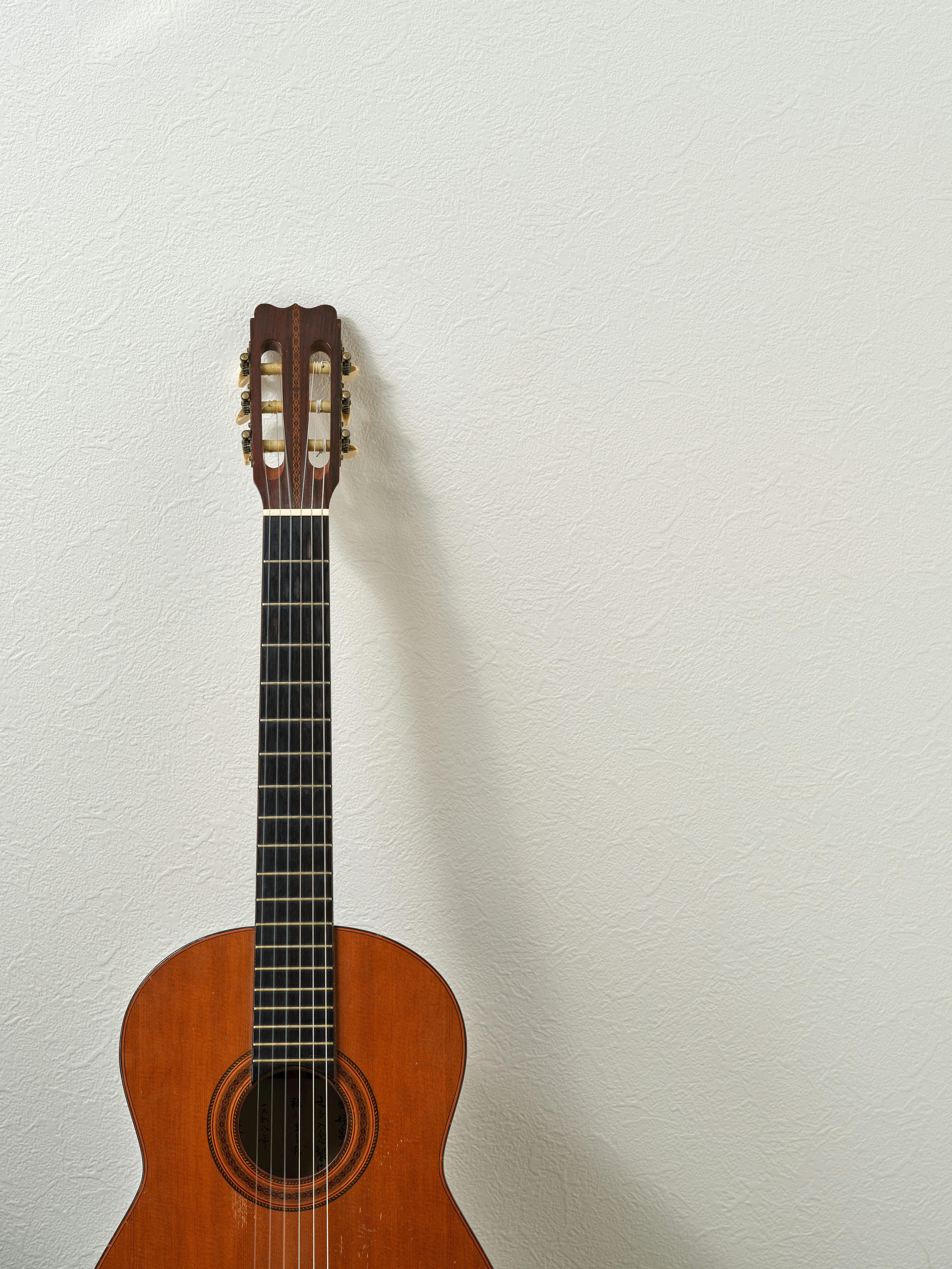 Una chitarra classica marrone appoggiata a un muro bianco