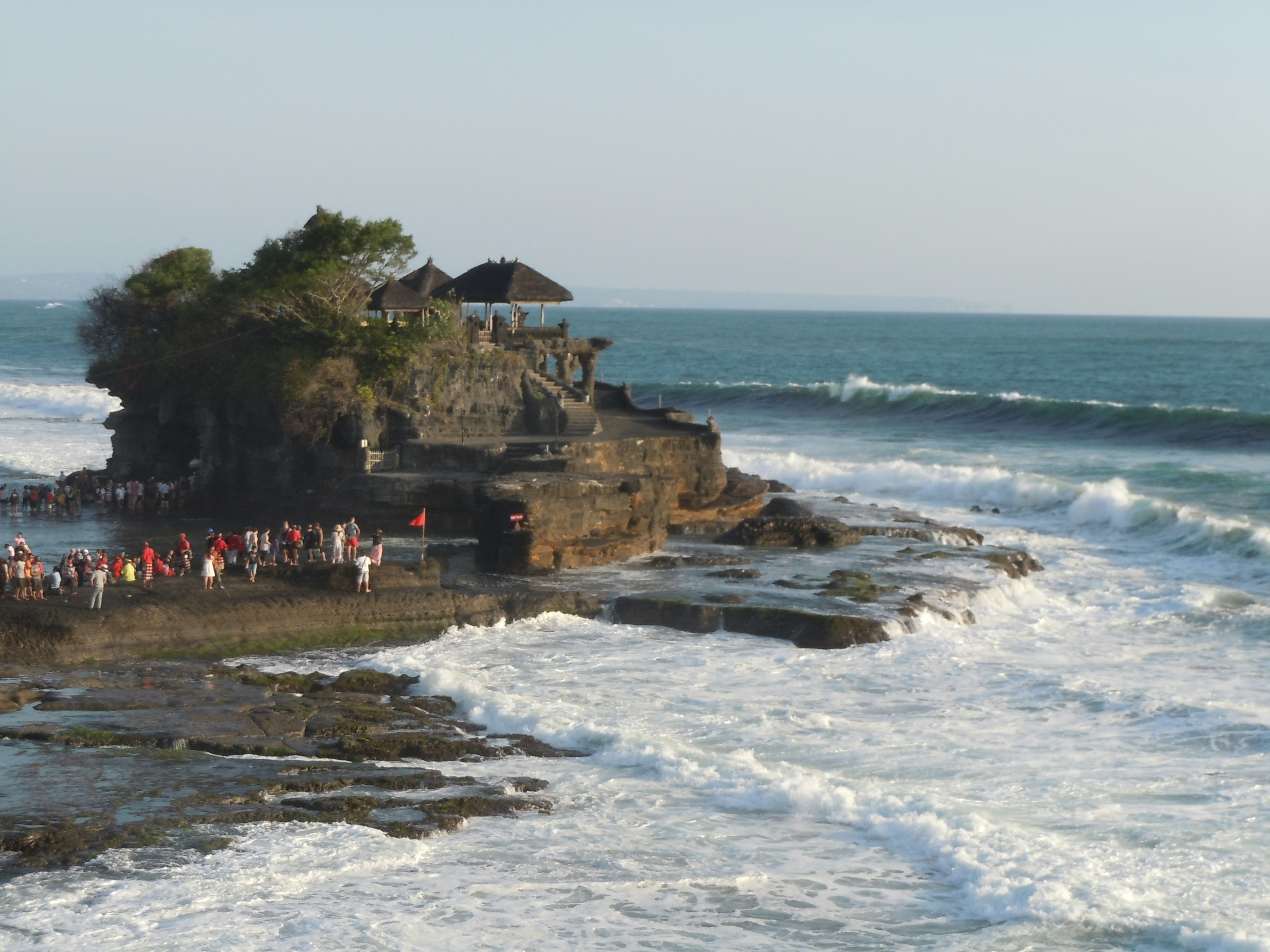 Vue panoramique du temple Tanah Lot avec des vagues déferlantes et des visiteurs