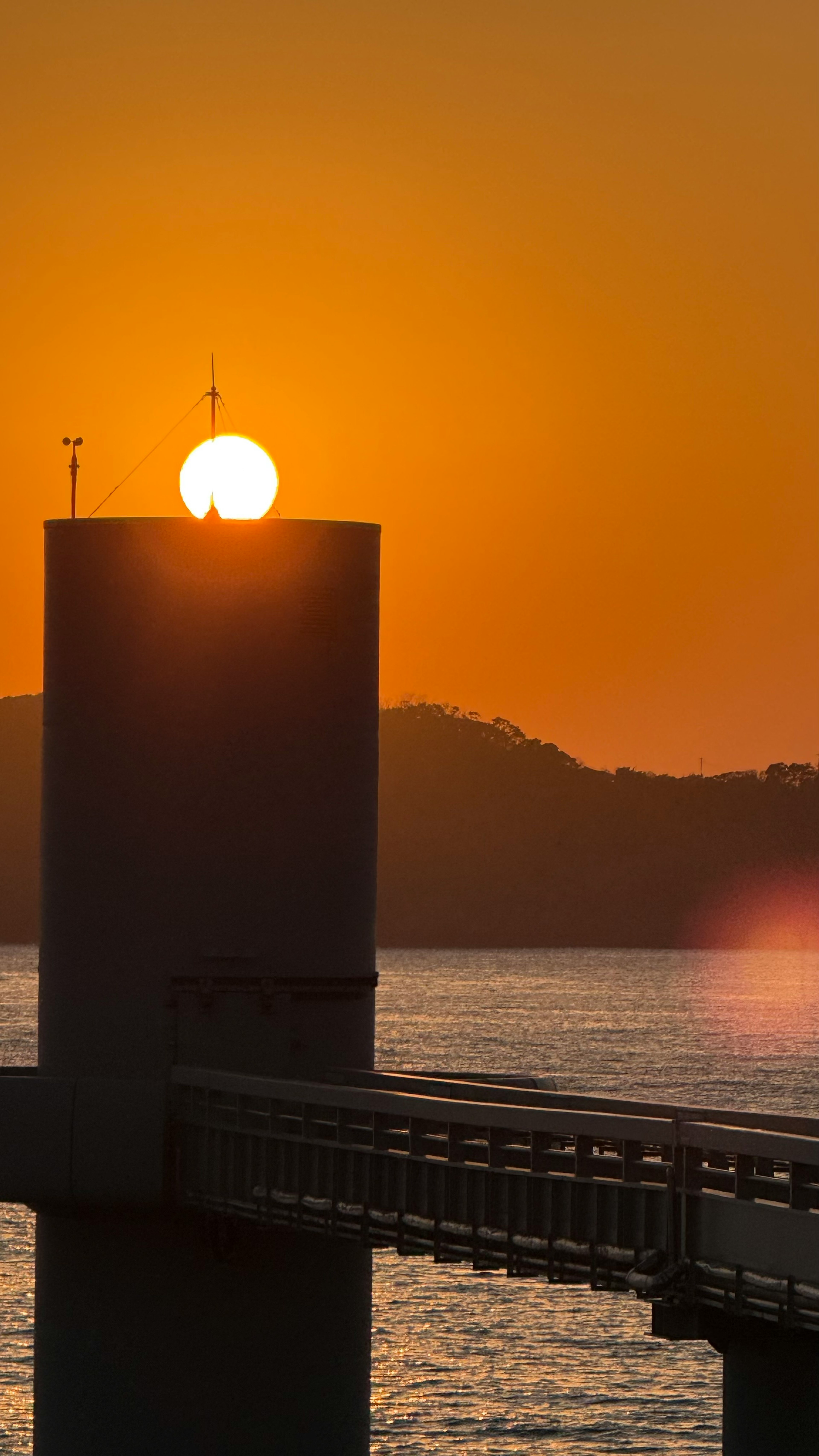 Silhouette di un faro con il tramonto che si riflette sull'acqua