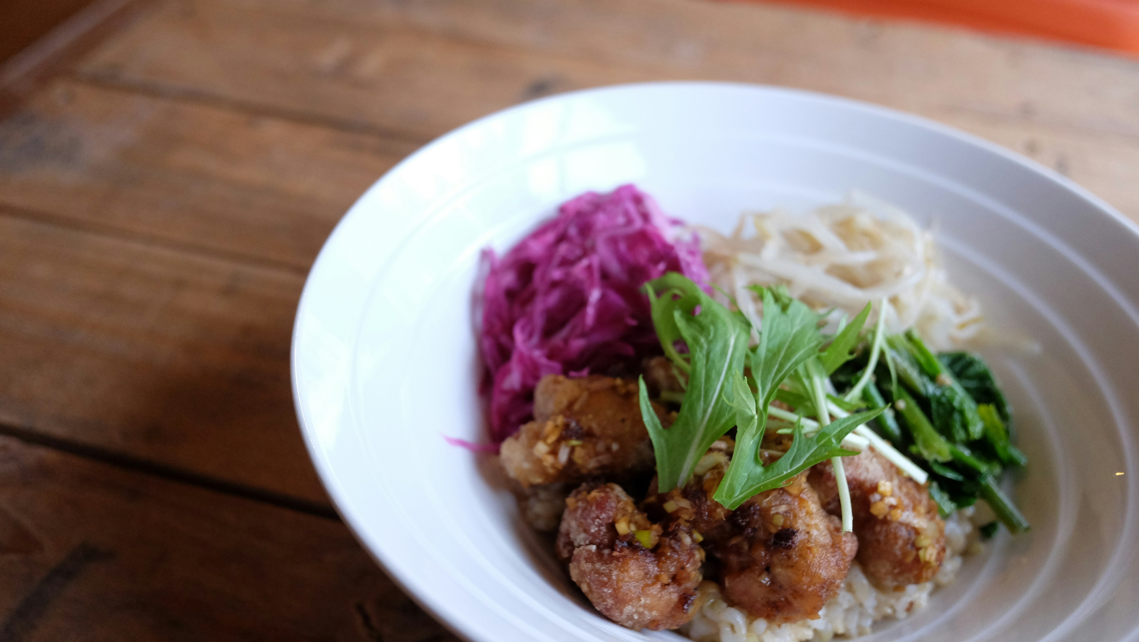 A dish on a white plate featuring purple cabbage green herbs rice noodles and round meatballs