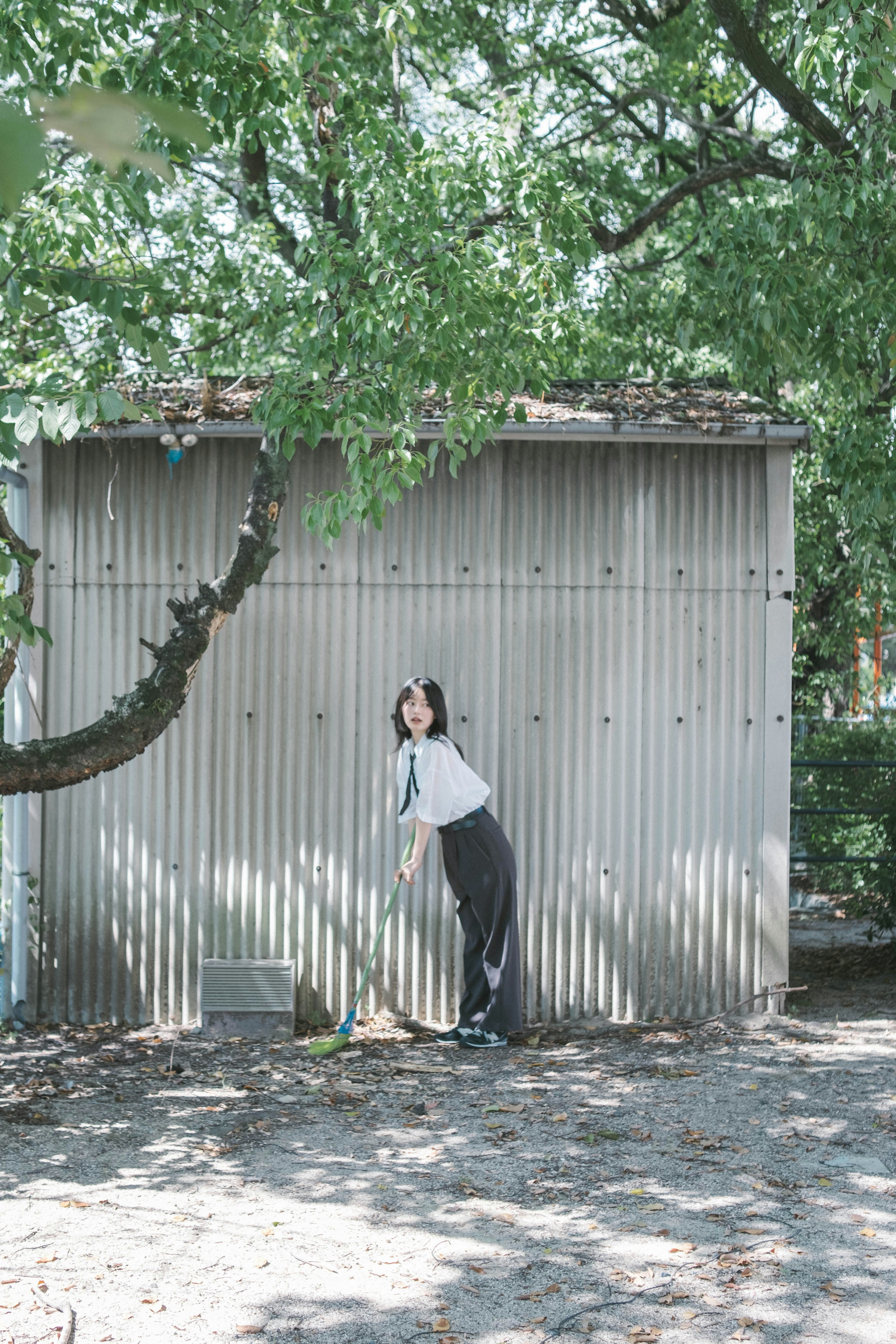 緑の木々の下で金属製の建物に寄りかかる女性の姿