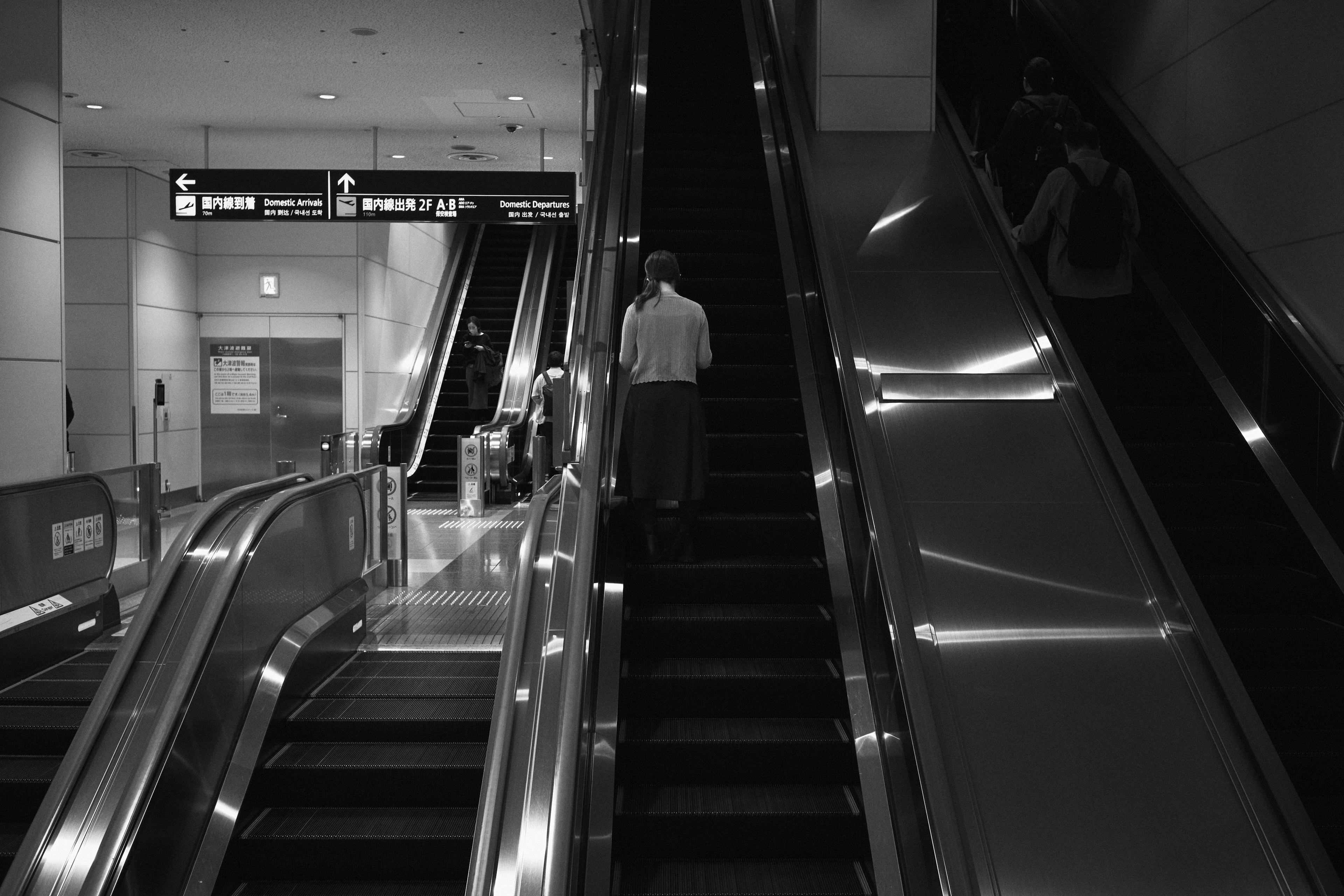 Eine Person, die in einem Raum mit Rolltreppen und Treppen in Schwarzweiß geht