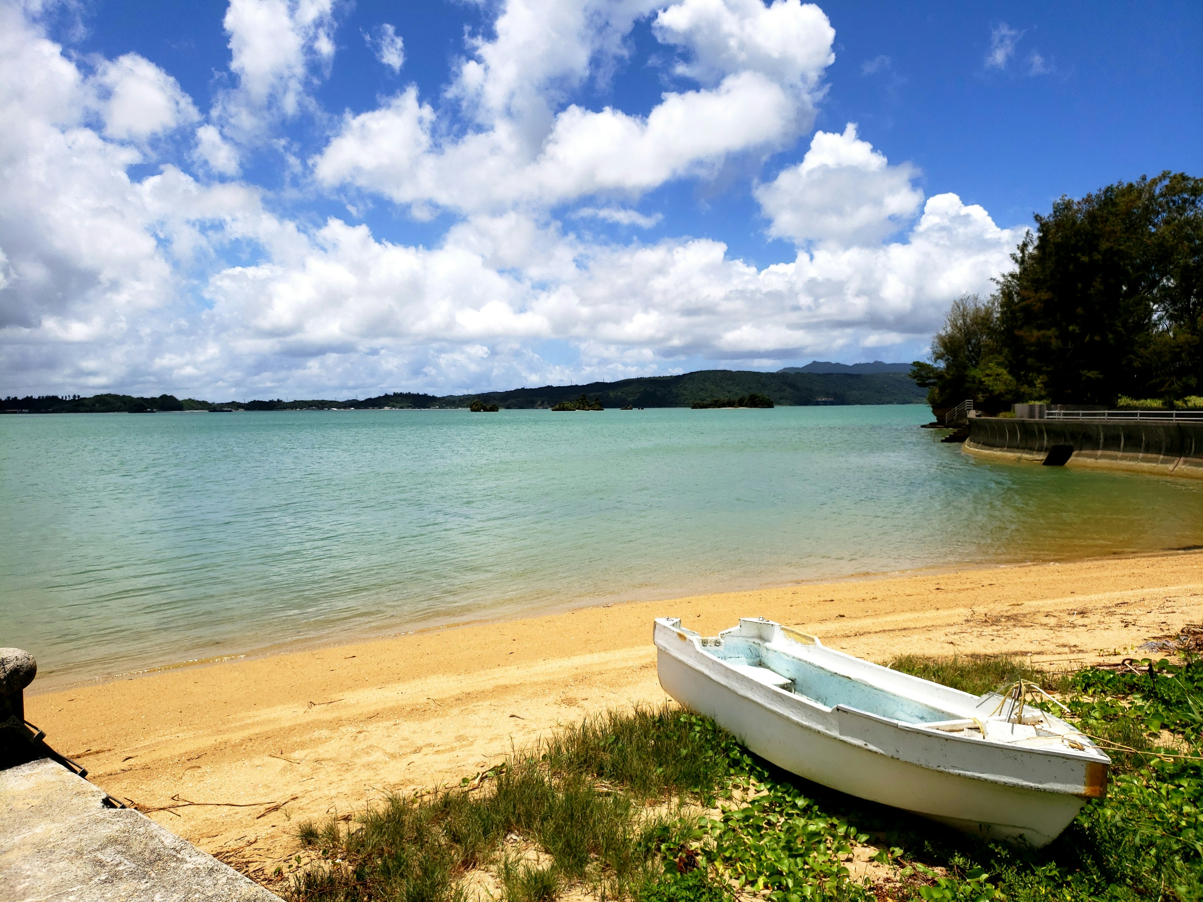 Ruhige Strandszene mit weißem Sand und ruhiger See Ein kleines Boot an der Küste Angeschnitten blauer Himmel mit flauschigen Wolken