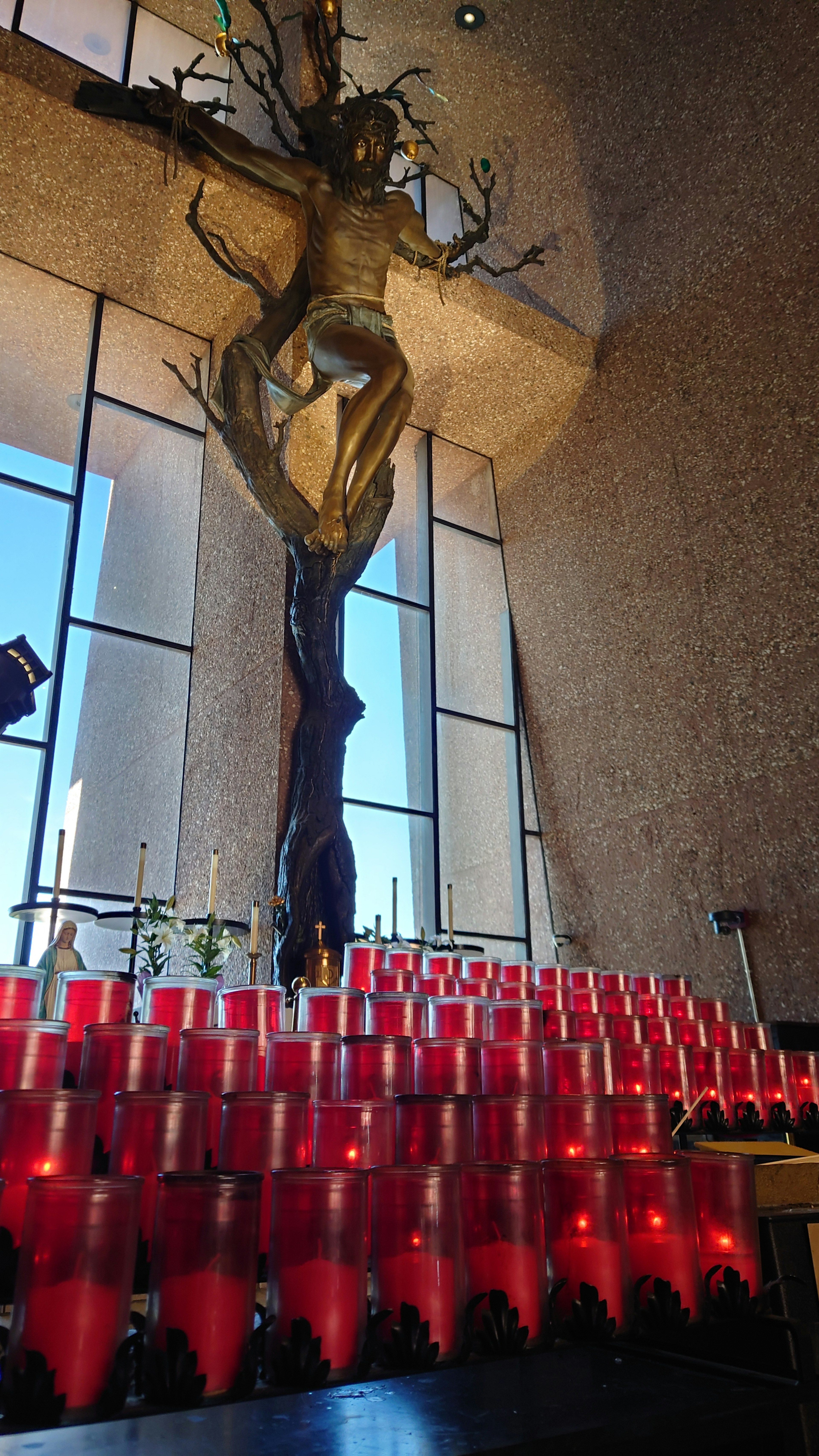 Interior de una iglesia con una gran escultura de madera y filas de velas rojas