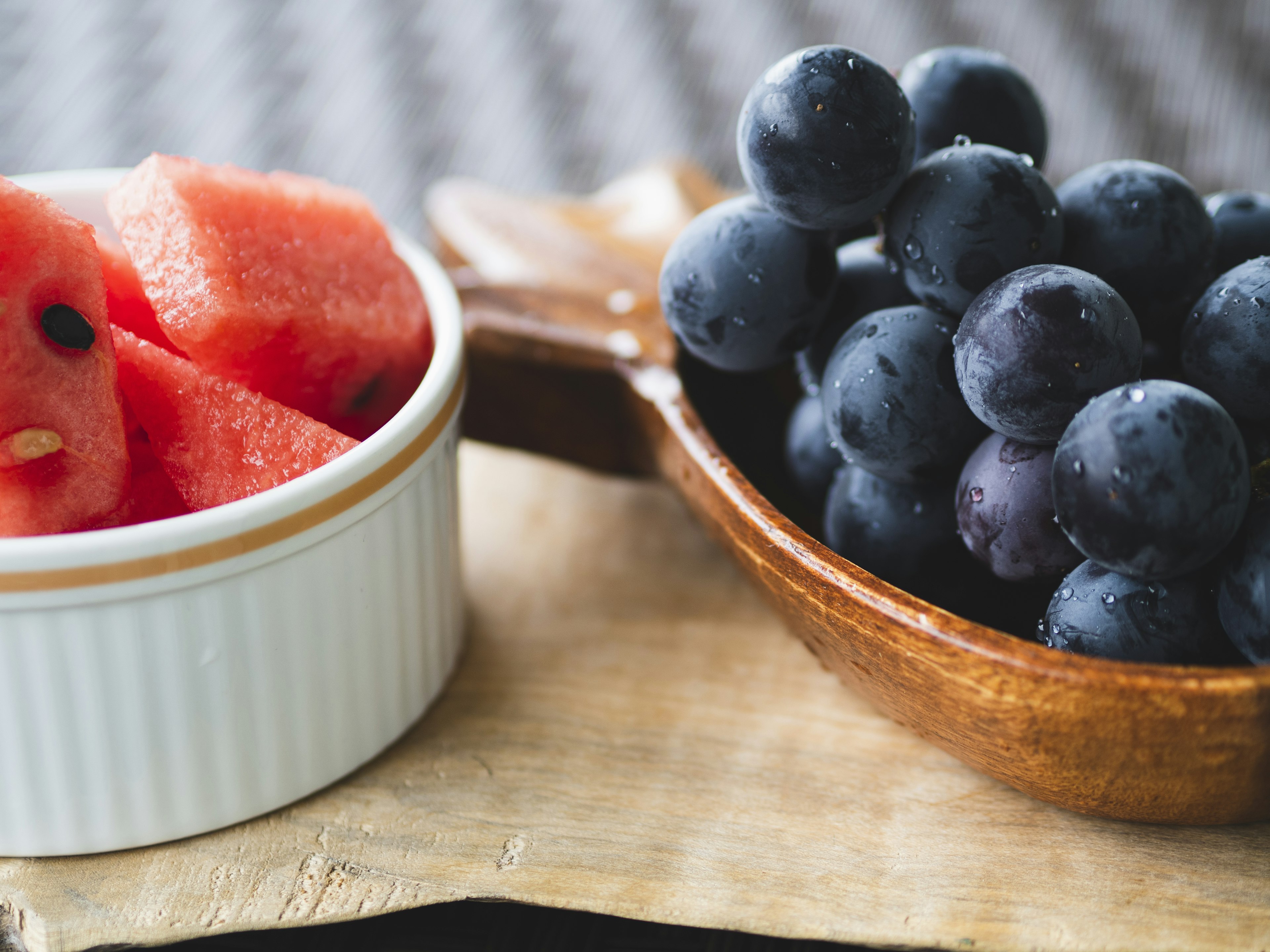 Stylish wooden plate with black grapes and sliced watermelon